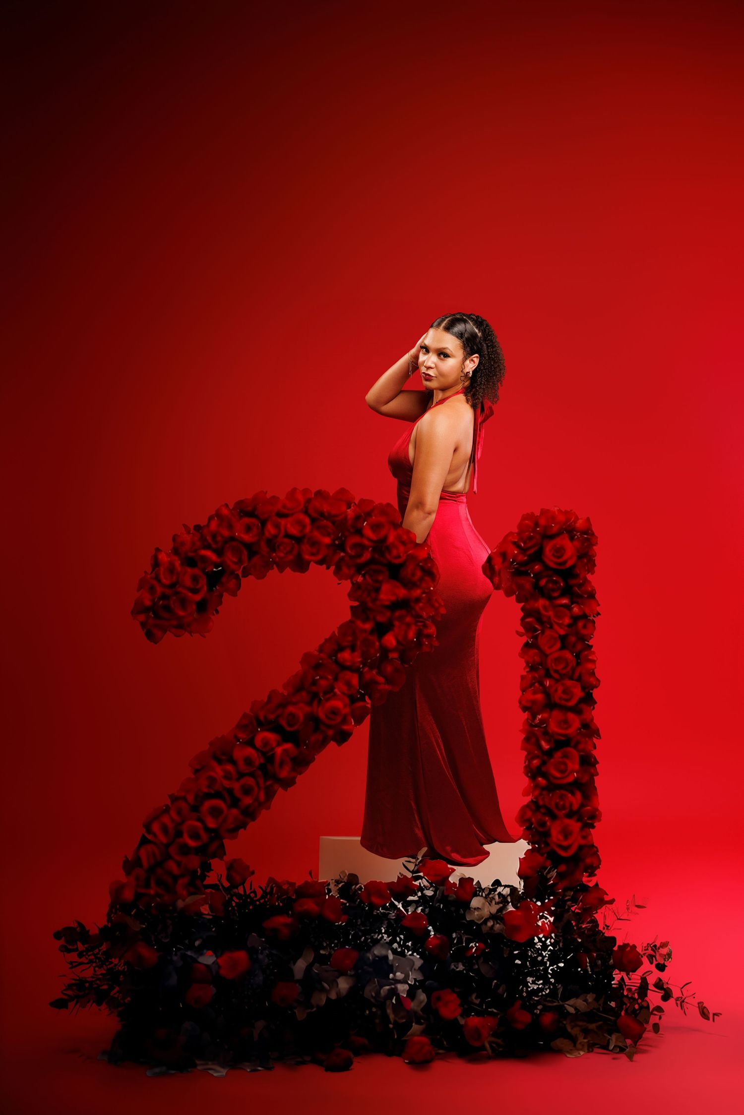 A woman in a red dress poses artistically in front of a red backdrop with dark floral decorative elements.
