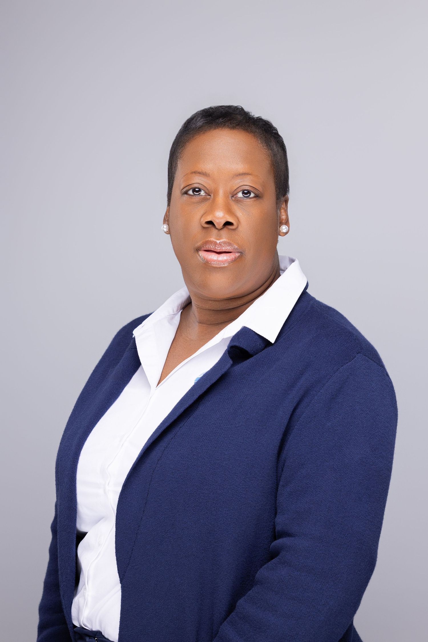 Professional headshot of someone in a navy blazer and white collared shirt against a gray background.