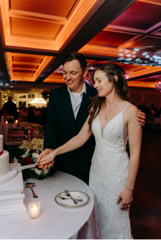 Couple cutting their wedding cake together at an elegant indoor reception with warm lighting and coffered ceiling.