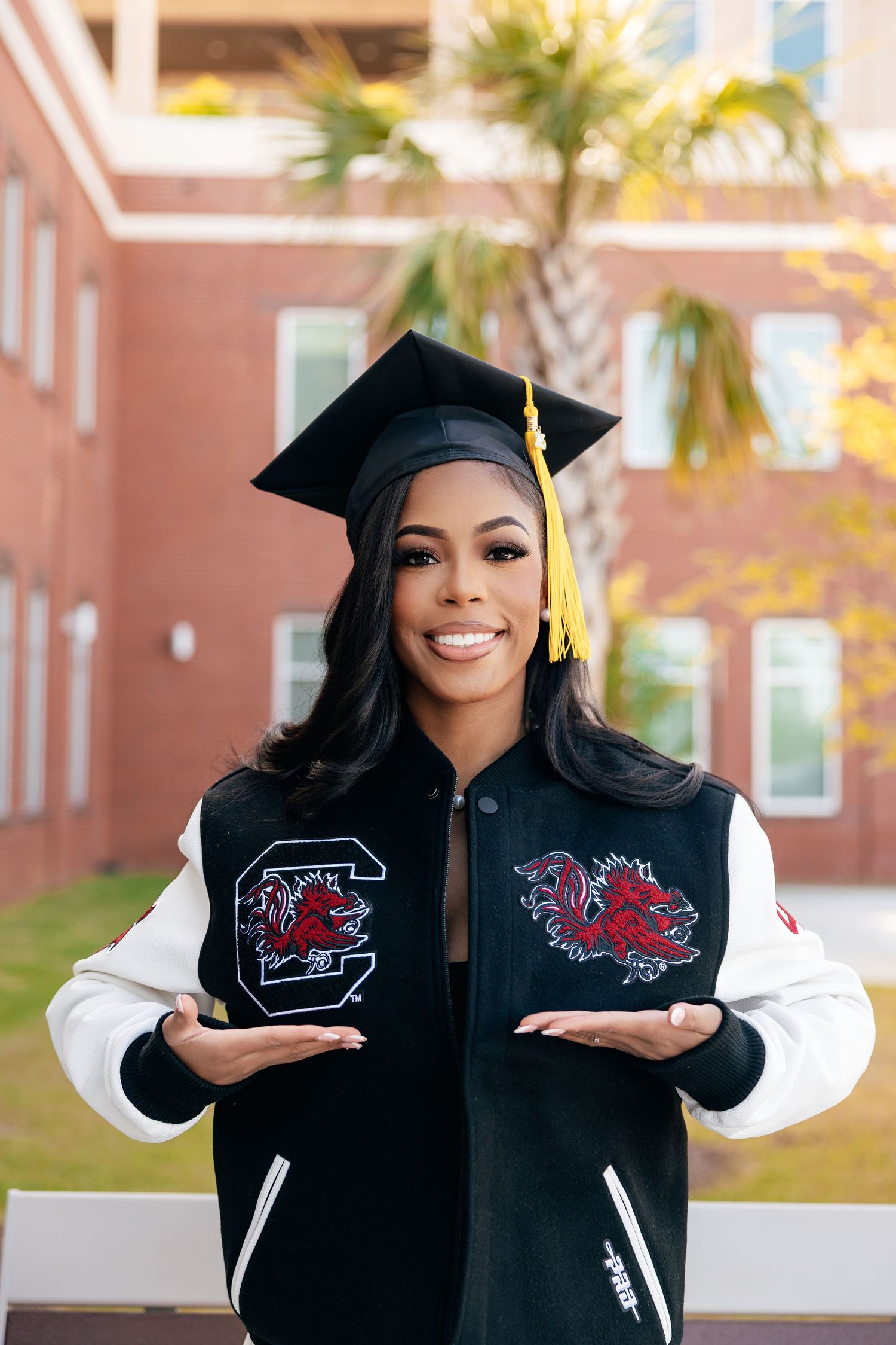 Graduate wearing academic regalia shows off university logos during outdoor graduation photo shoot.