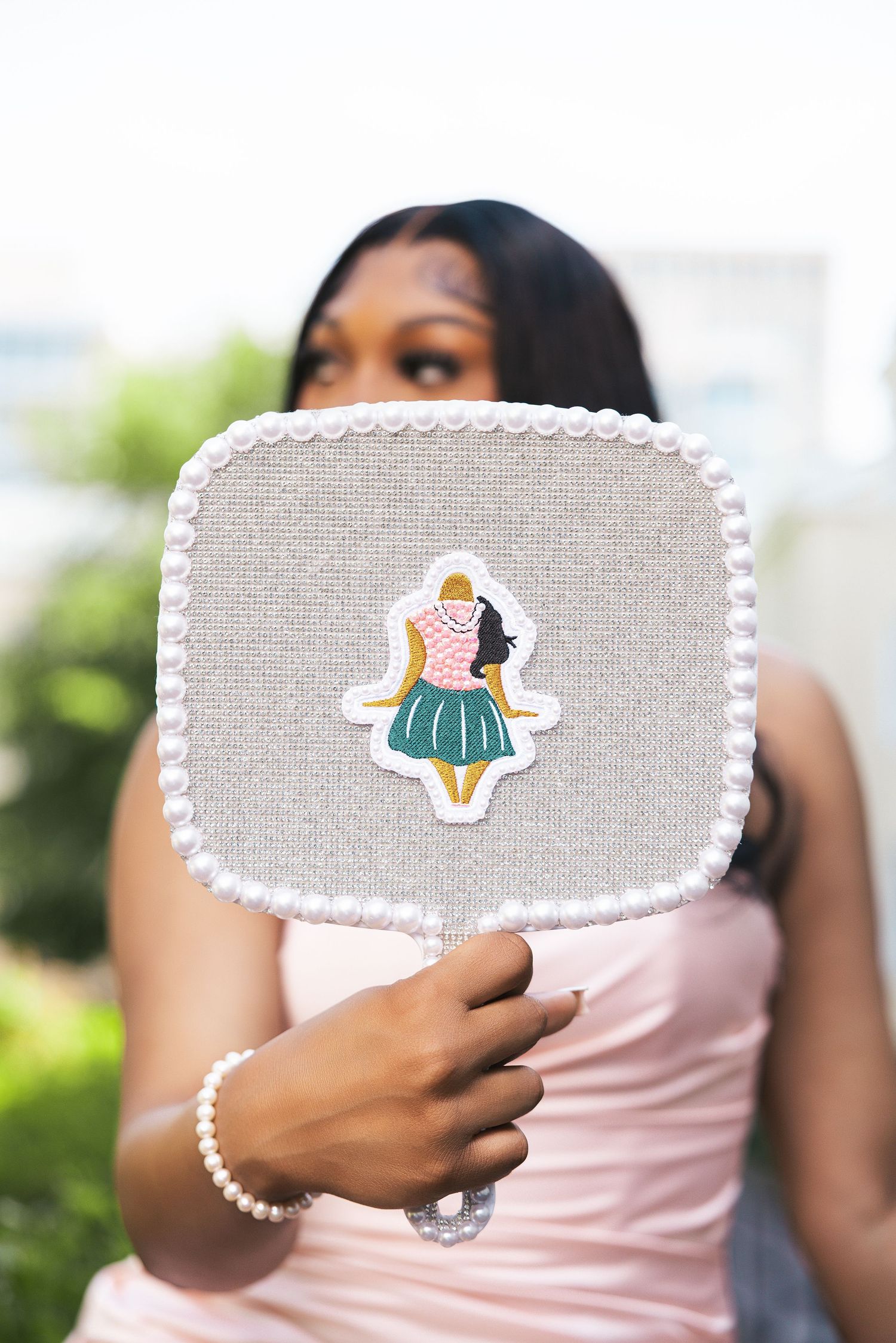 Hand holds decorative fabric square with pom-pom trim and cute illustrated patch.