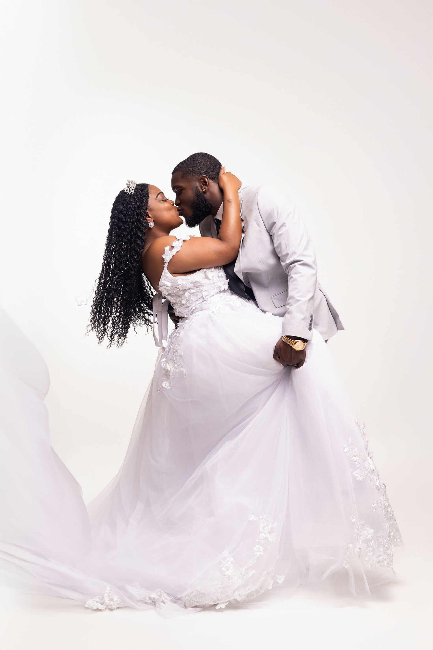 Romantic dip pose of couple in white wedding attire against light background.