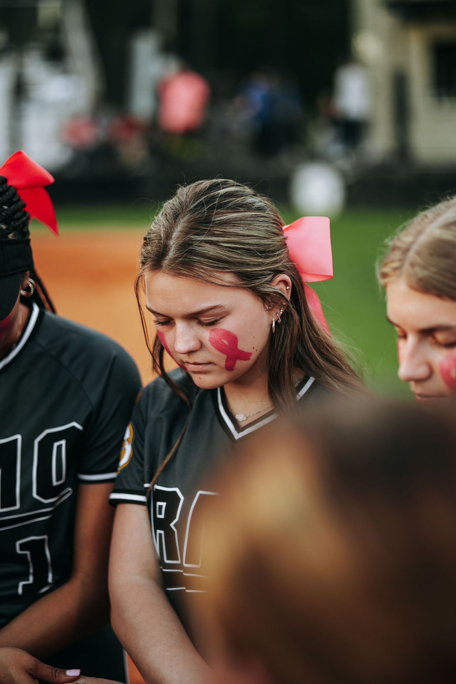 Softball team players huddled together wearing black uniforms with pink ribbons.