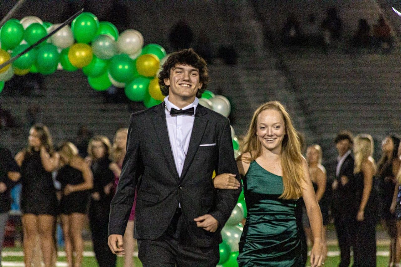 Students celebrating in formal attire at a school event with green balloons decorating the venue.