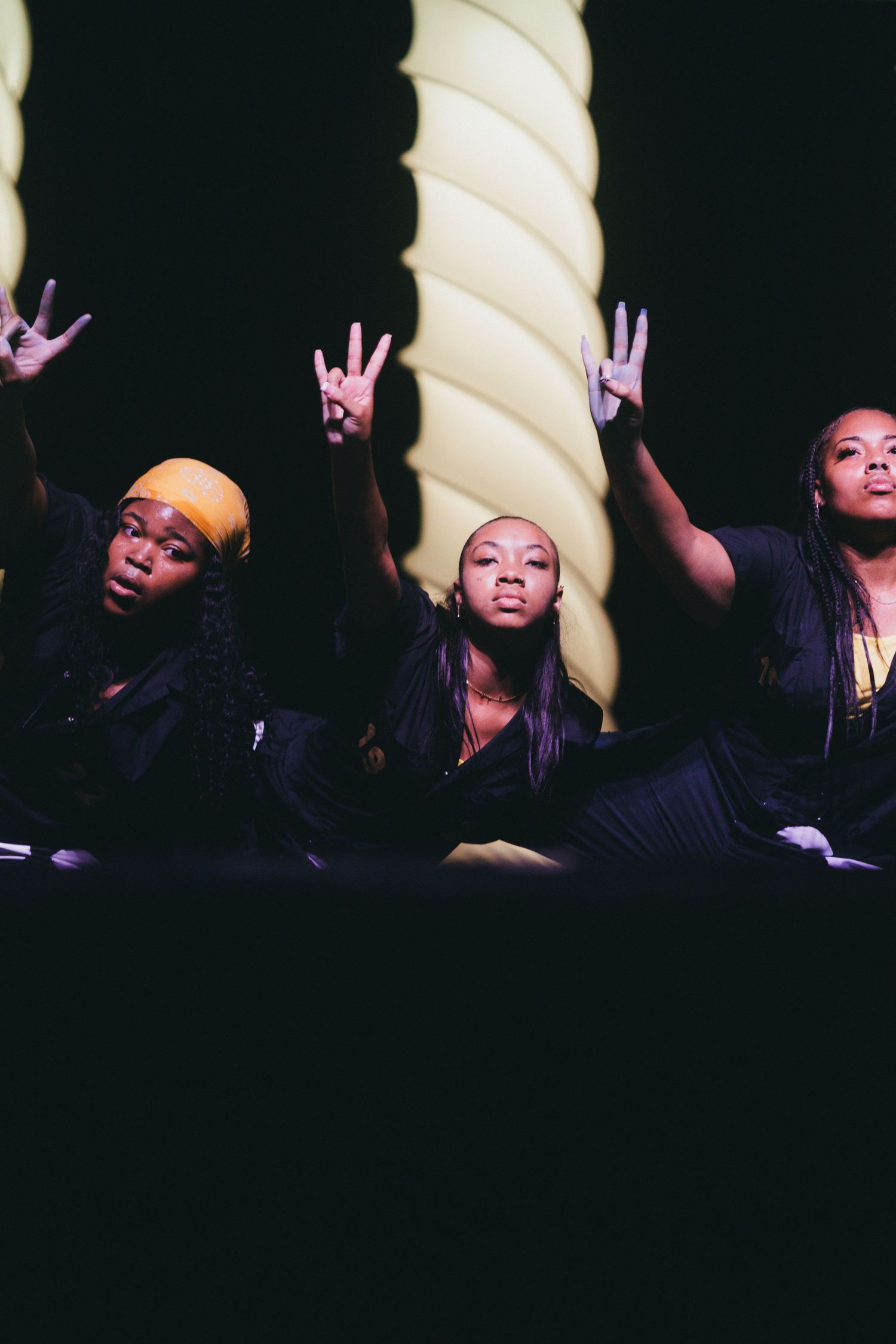 Several dark silhouettes of SGROHS gesturing with peace signs against a black background with spiral decor visible.