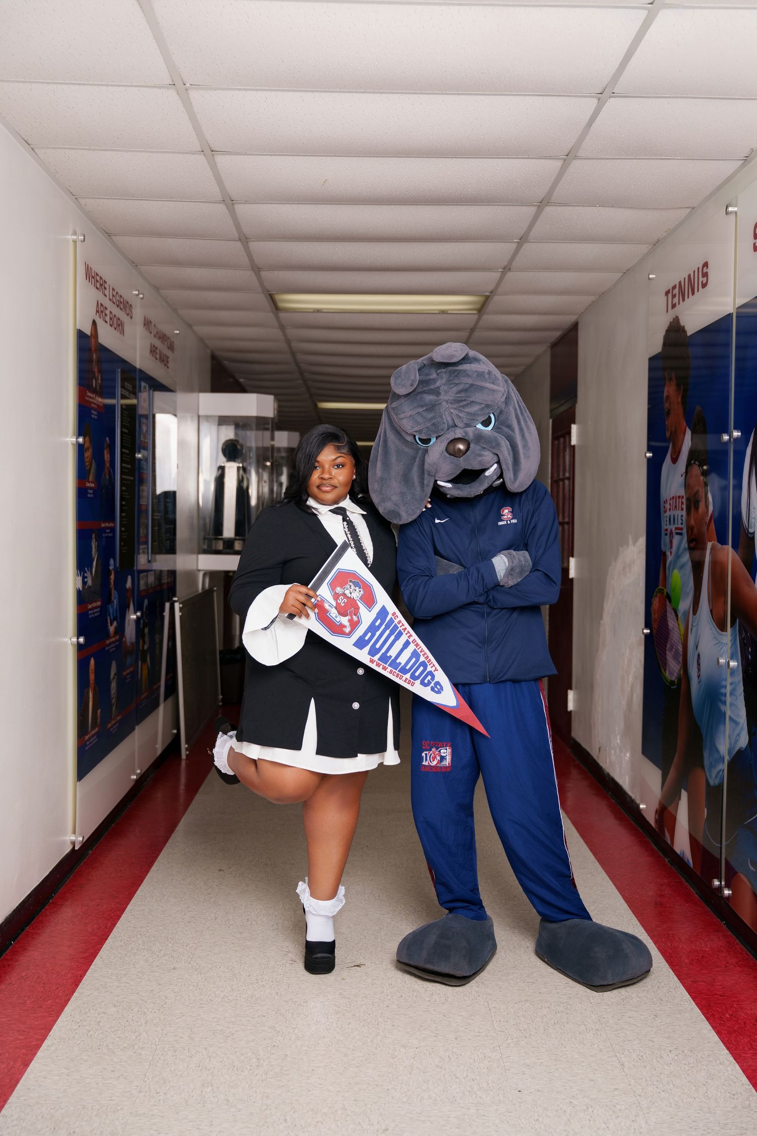 Student poses with Bulldogs mascot in school hallway, holding a pennant, wearing matching Bulldogs themed outfits.