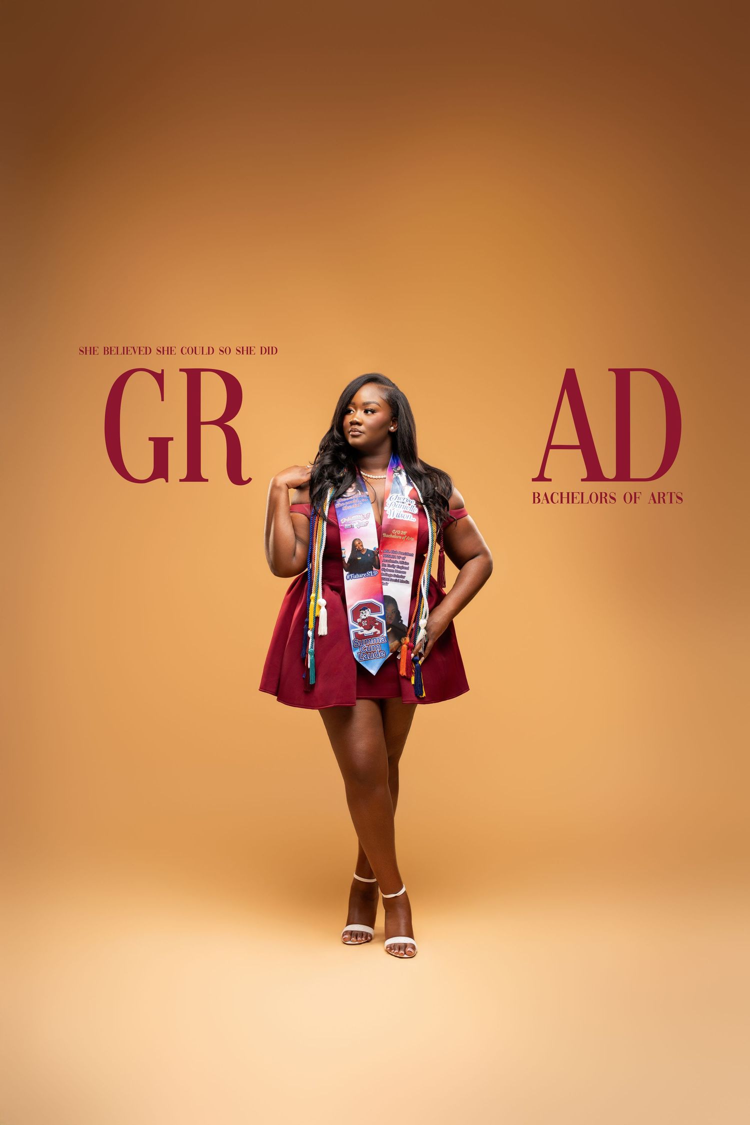 Young woman in red graduation dress and stole poses for GRAD Bachelors of Arts celebration photo on orange background.