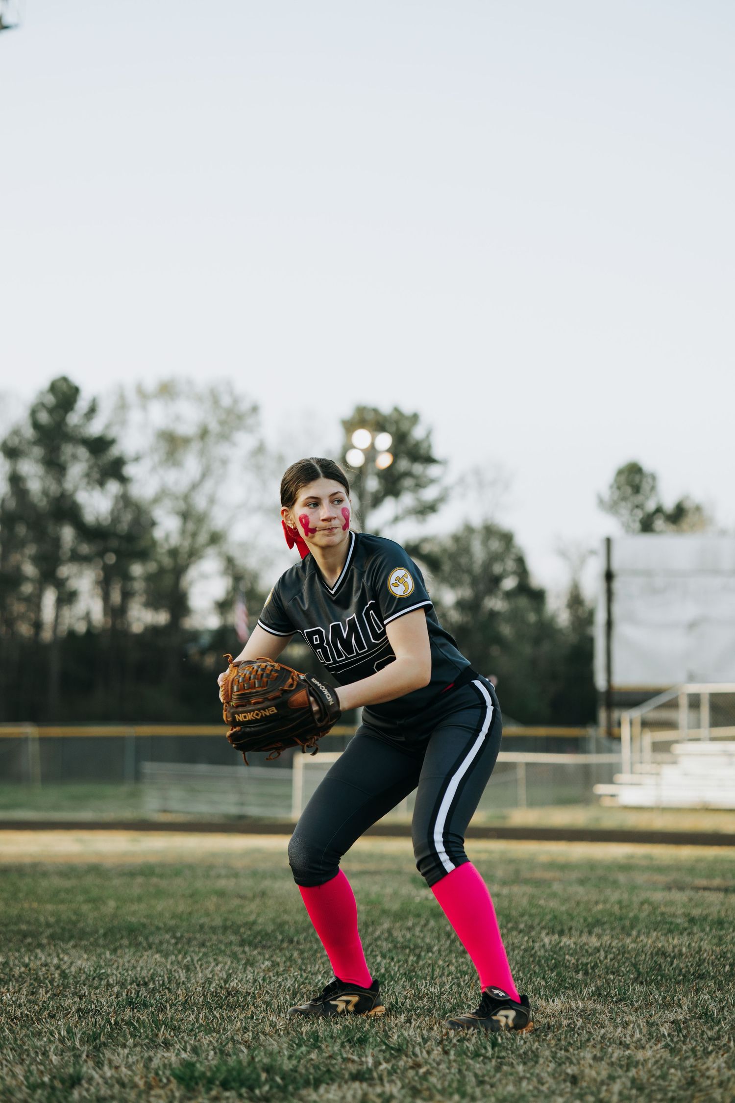 Irmo HS Softball player in black uniform and pink socks practicing fielding stance on grass field.