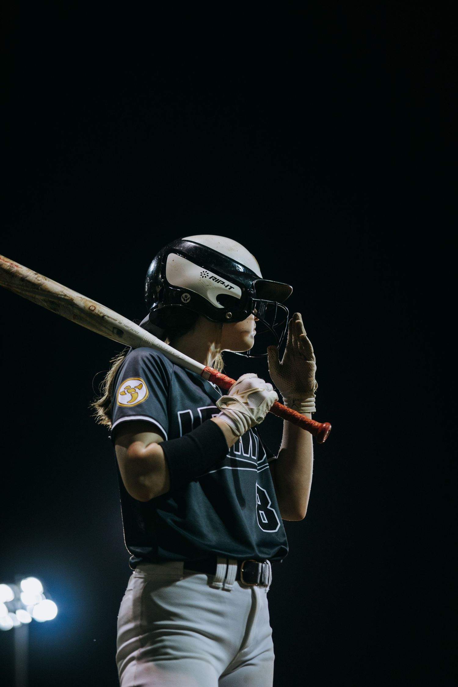 Baseball player adjusts batting helmet while holding bat at night game.
