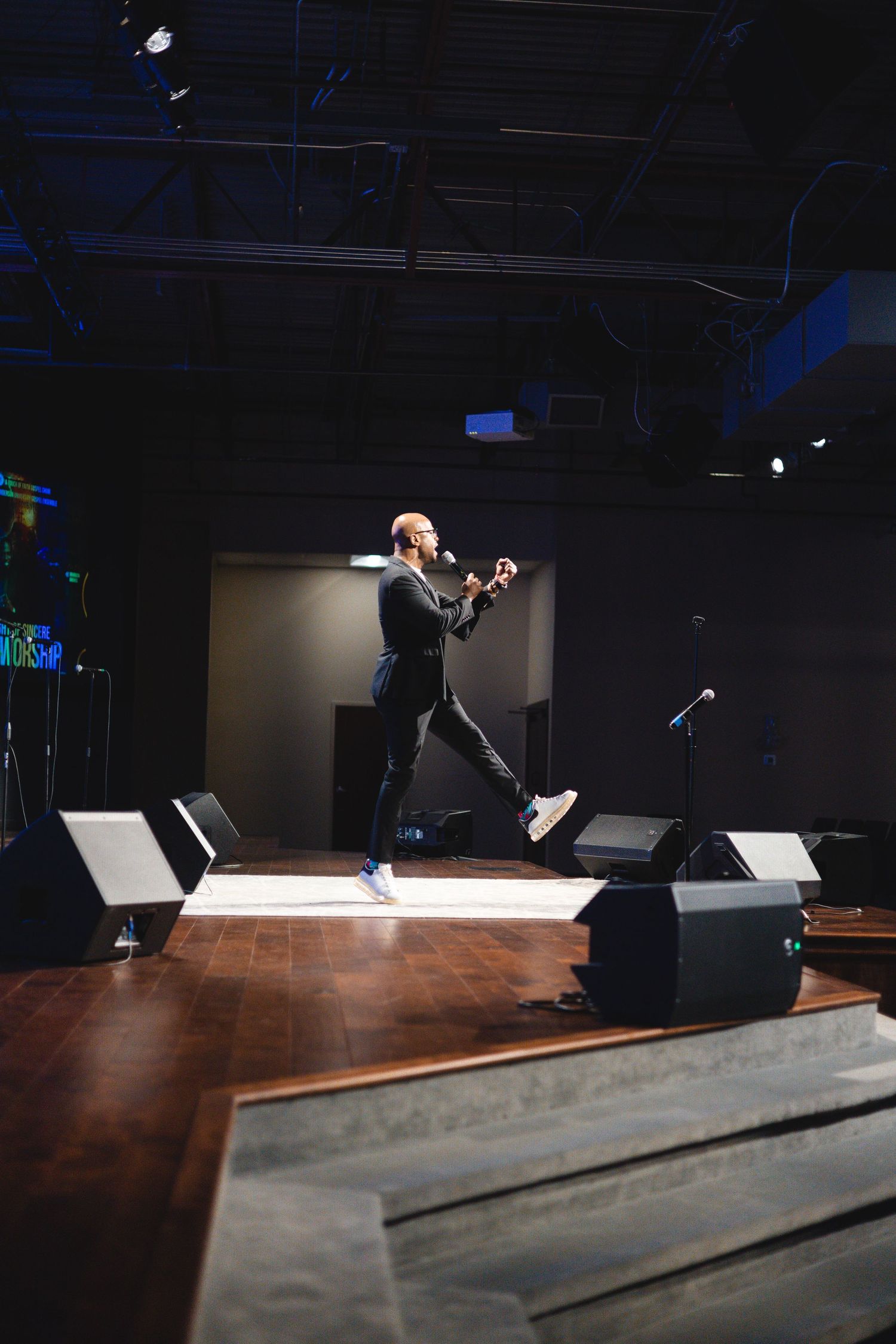 Dramatic wide shot of performer on wooden stage with theatrical lighting.