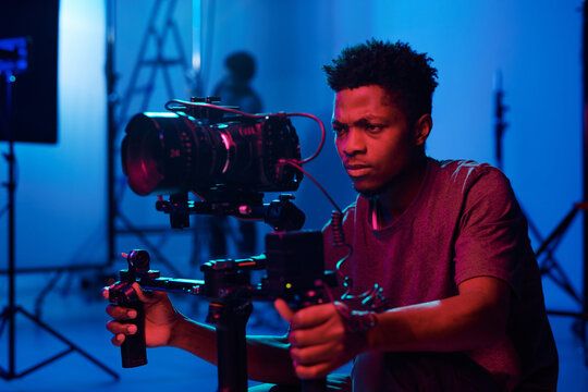 Cinematographer filming with professional camera equipment in blue-lit studio environment.