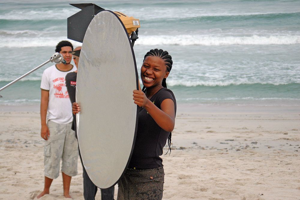 Two photographers working with lighting equipment and reflectors on a cloudy beach.