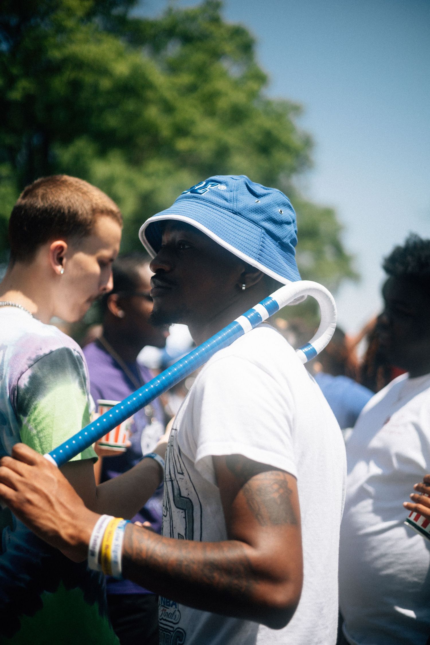 A person in a blue bucket hat and white t-shirt holds a blue pole at an outdoor gathering.  USC Hip Hop Wednesday