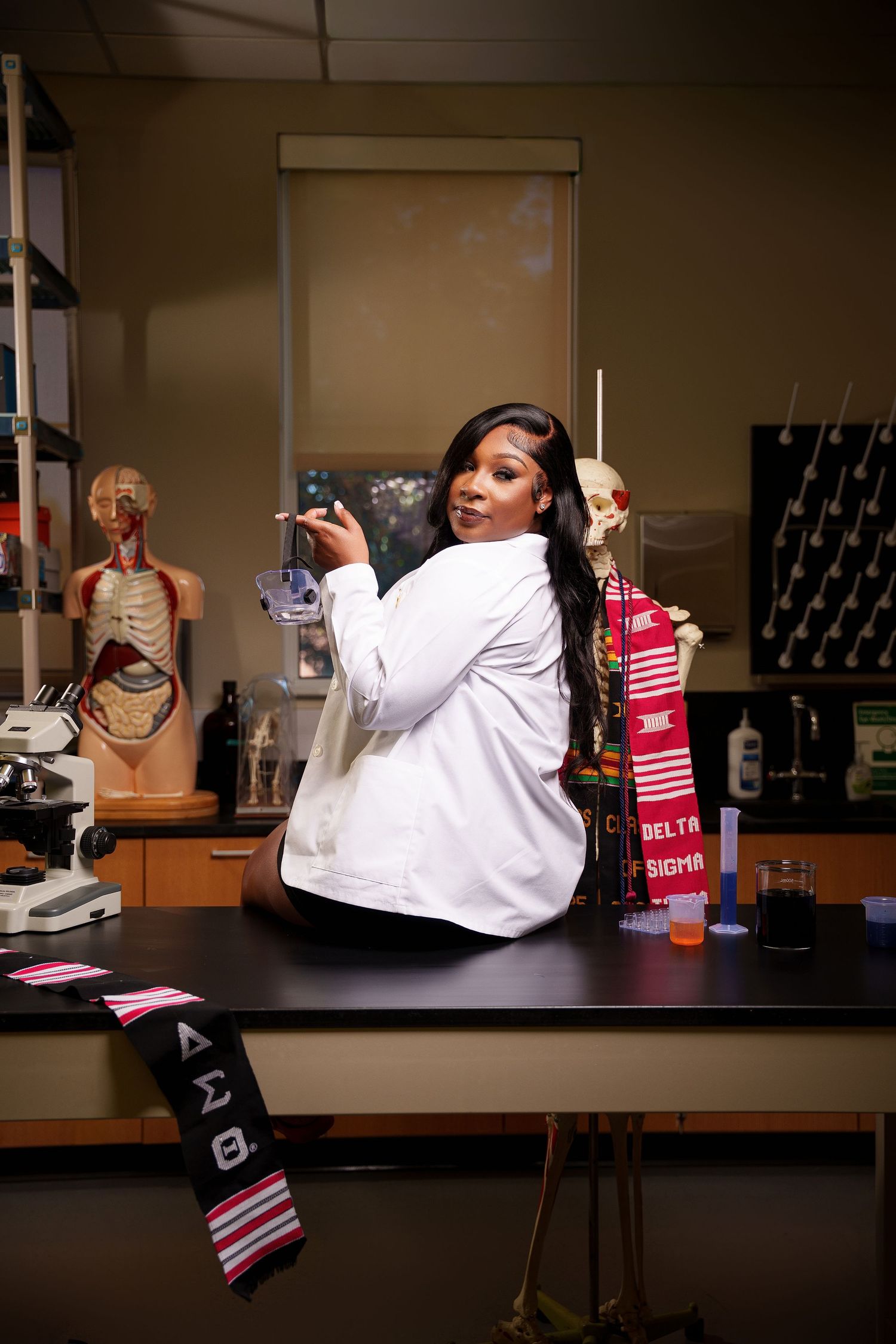 A medical professional in a white lab coat poses playfully in a laboratory setting with anatomical models and supplies.
