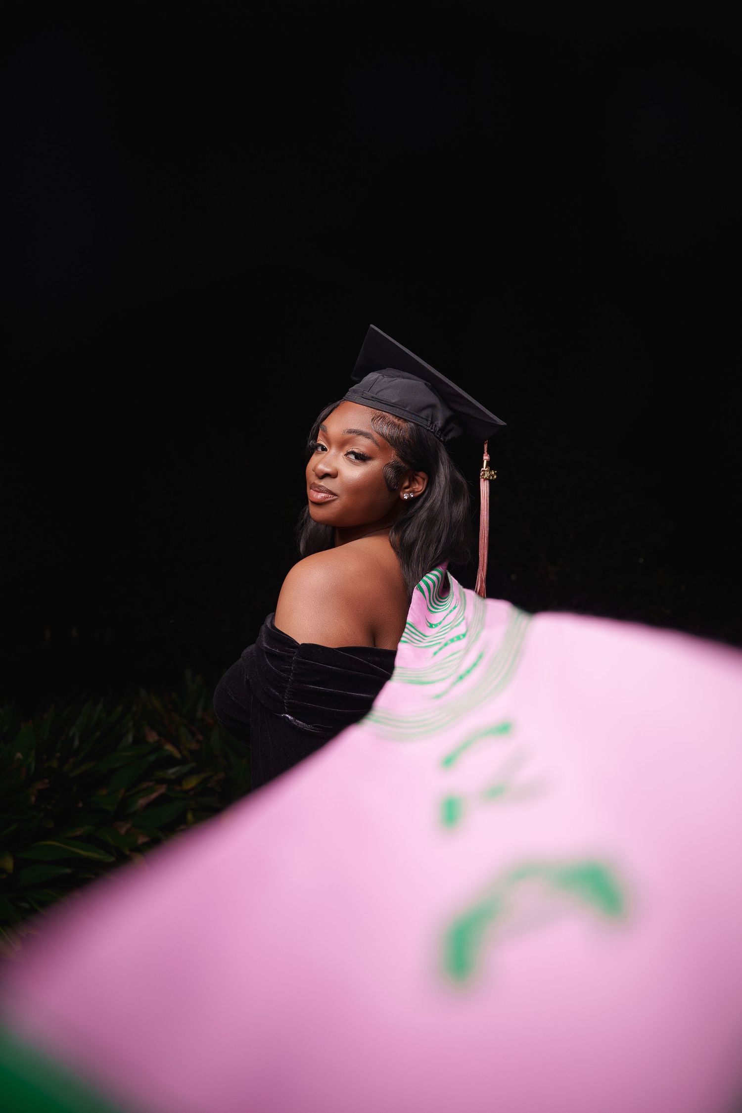 A graduation photoshoot featuring joyful expressions against a dark background with pink lighting effects.