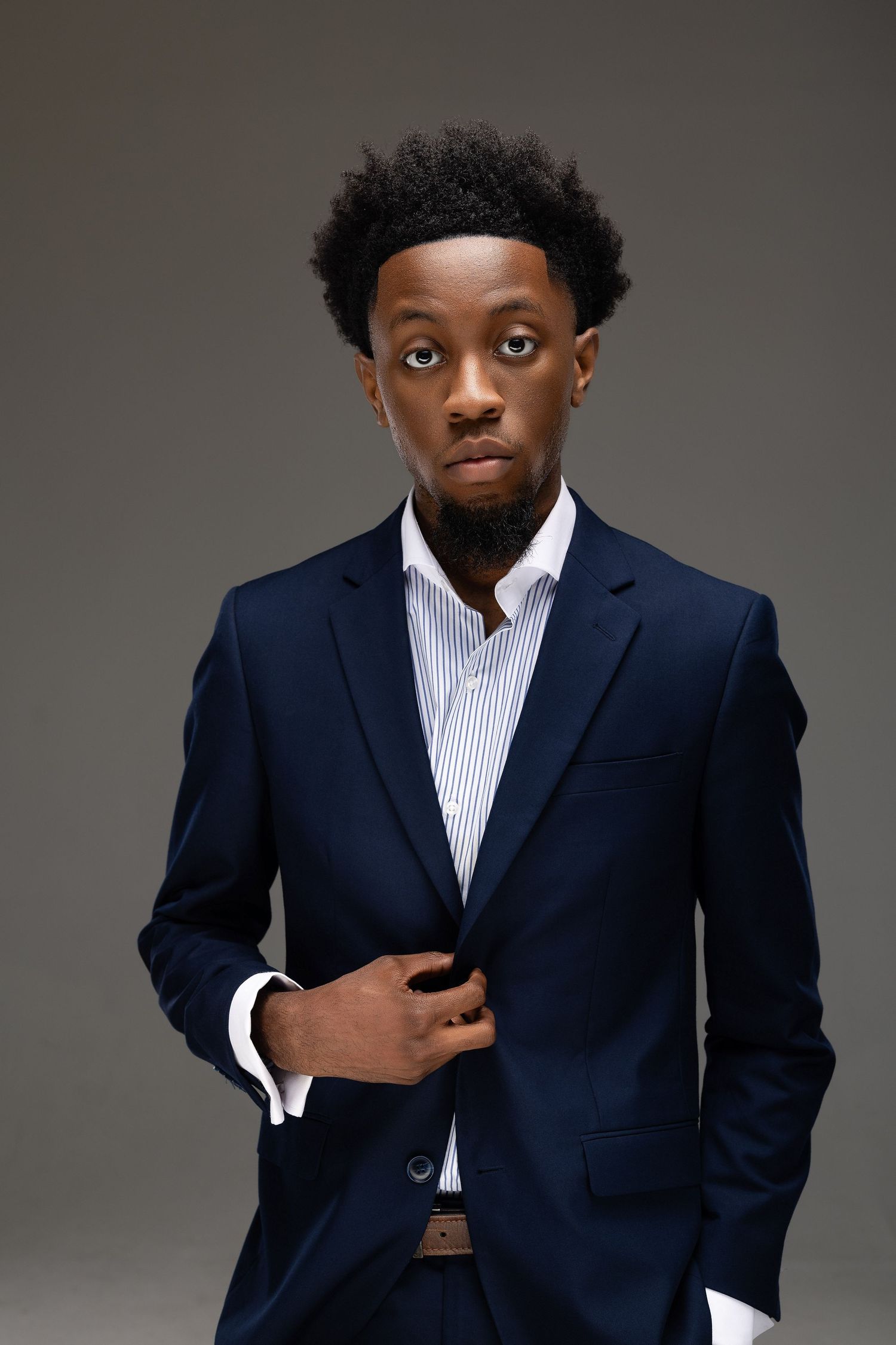 A person in a navy suit and striped shirt poses in multiple dynamic shots against a gray studio background.