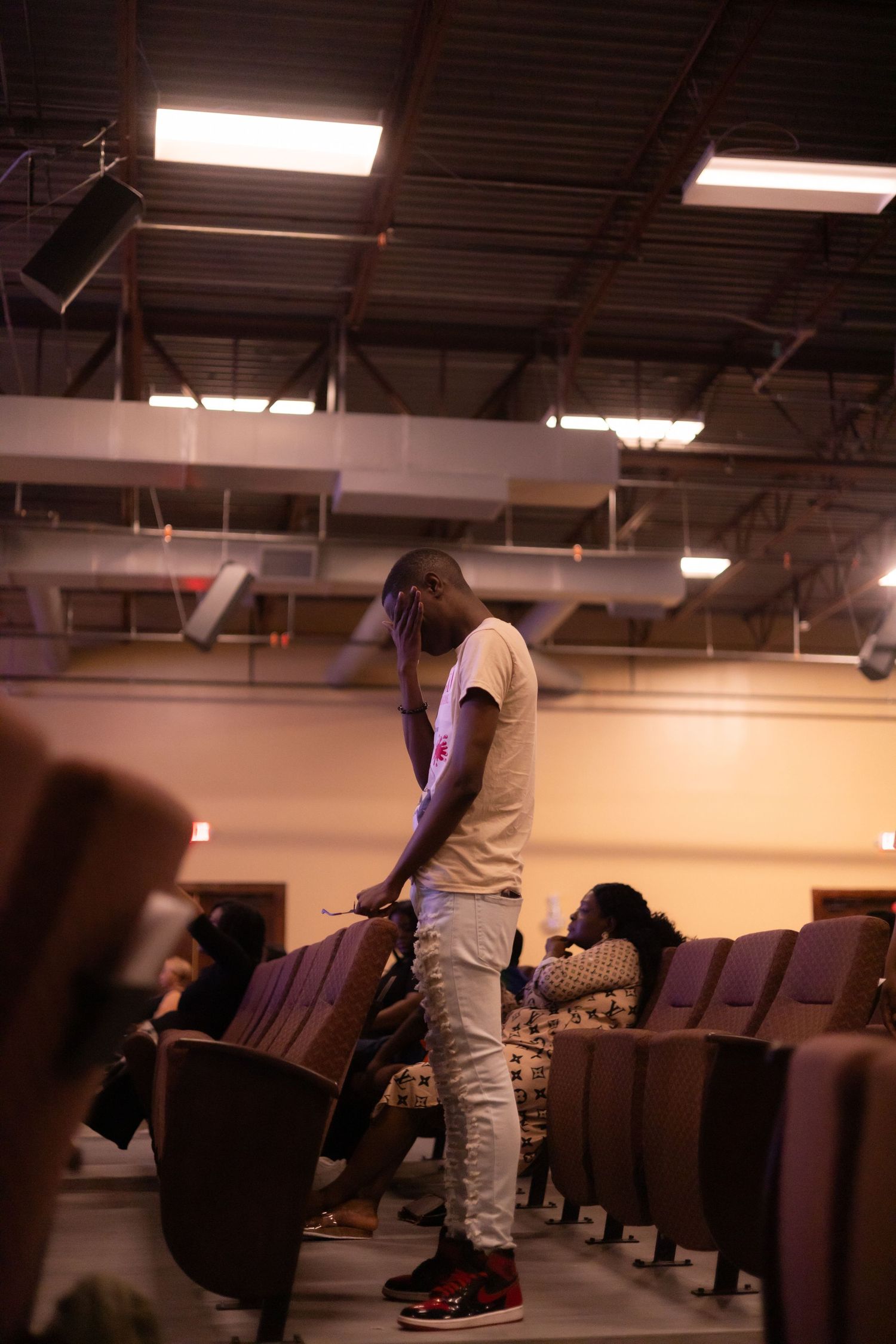 A person stands in an auditorium aisle between rows of theater-style seating under fluorescent lighting.