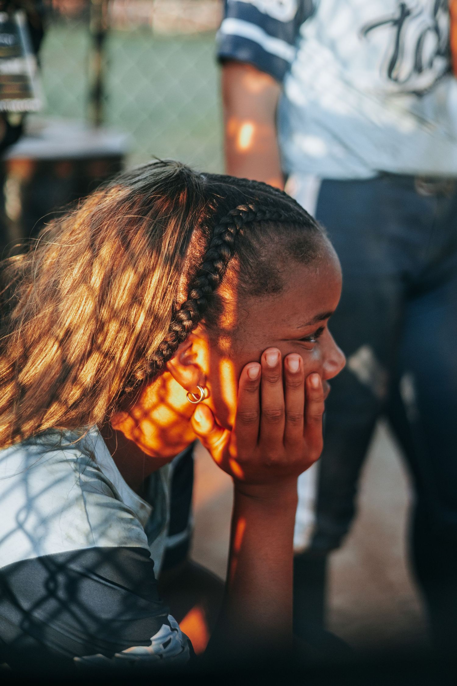 A softball player rests their head in their hands during sunset.