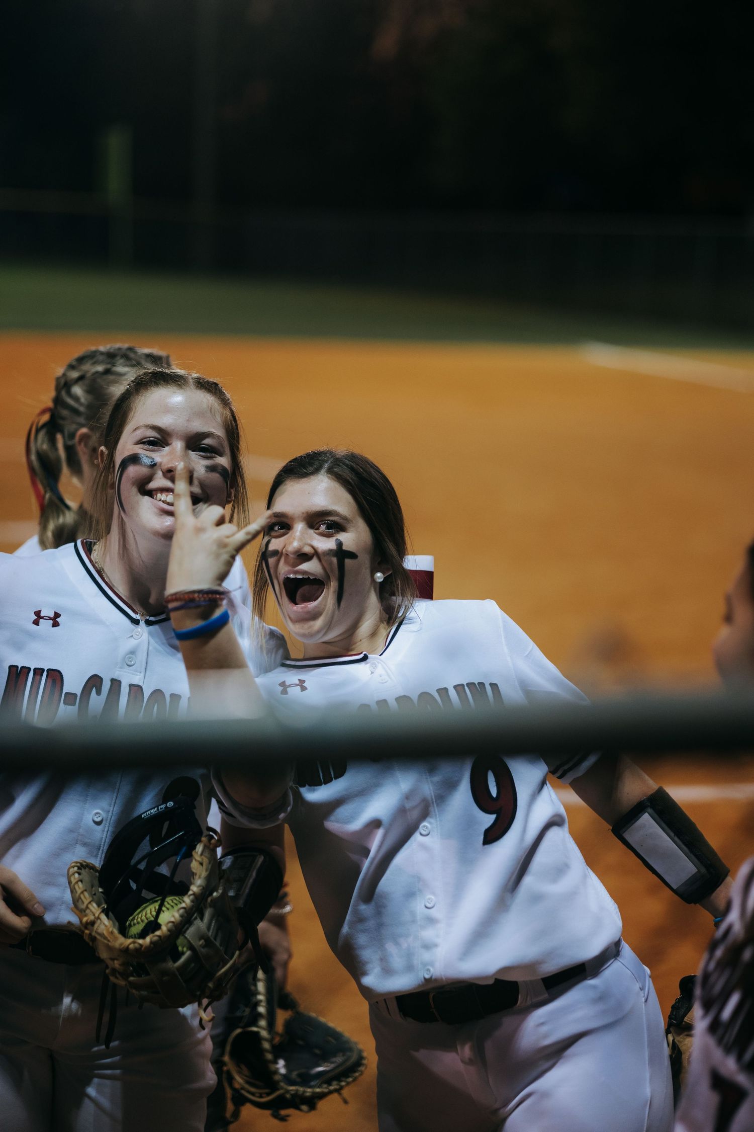 Softball teammates celebrate excitedly in dugout during game.