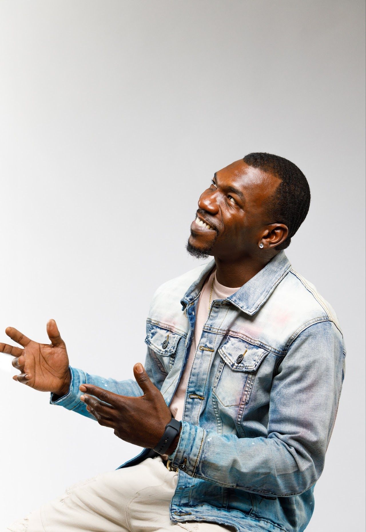 Person in light denim jacket gestures expressively while seated against white background.