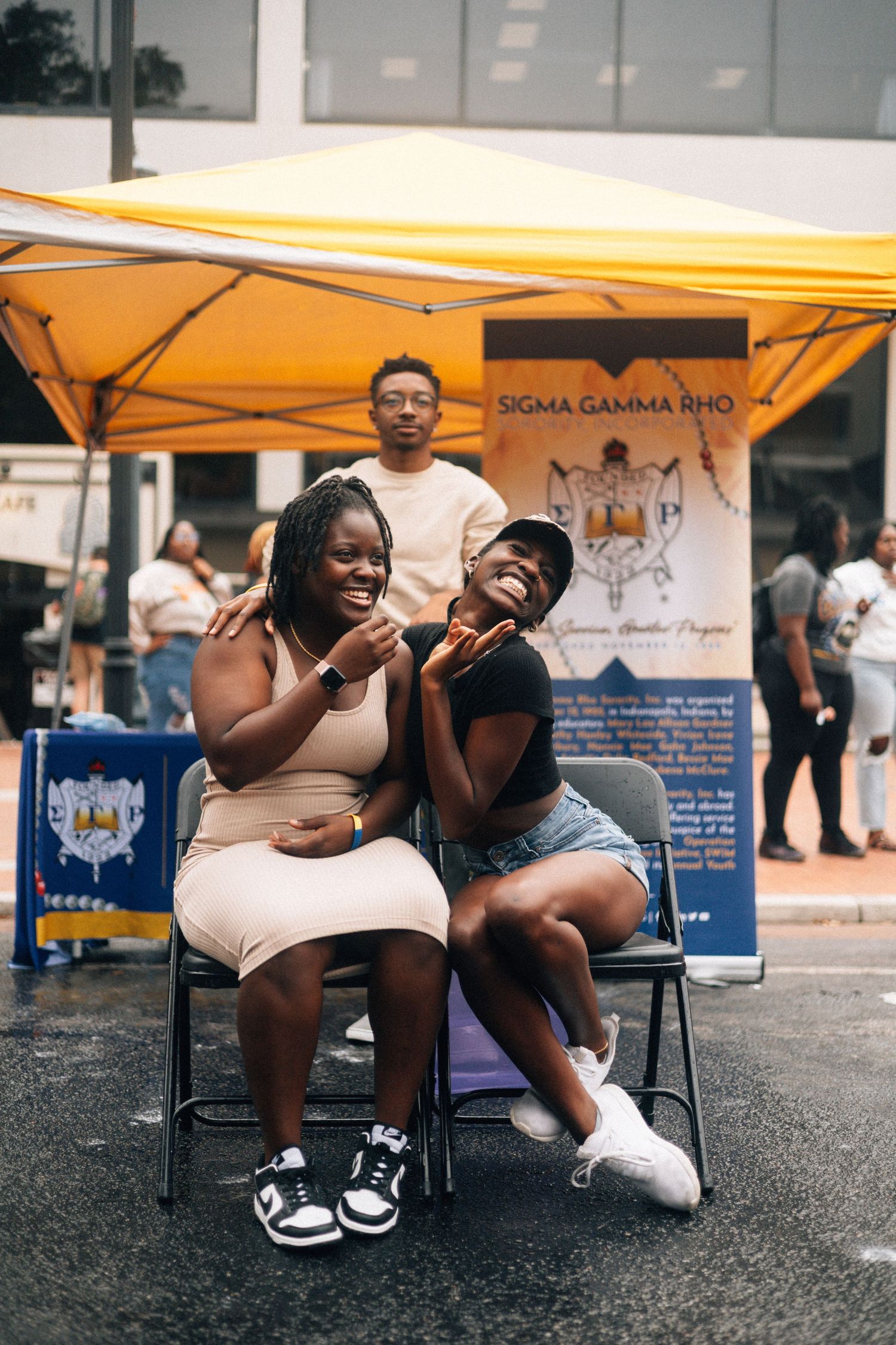 Five sequential images show people sitting under a yellow tent at an outdoor community event, captured in candid moments.