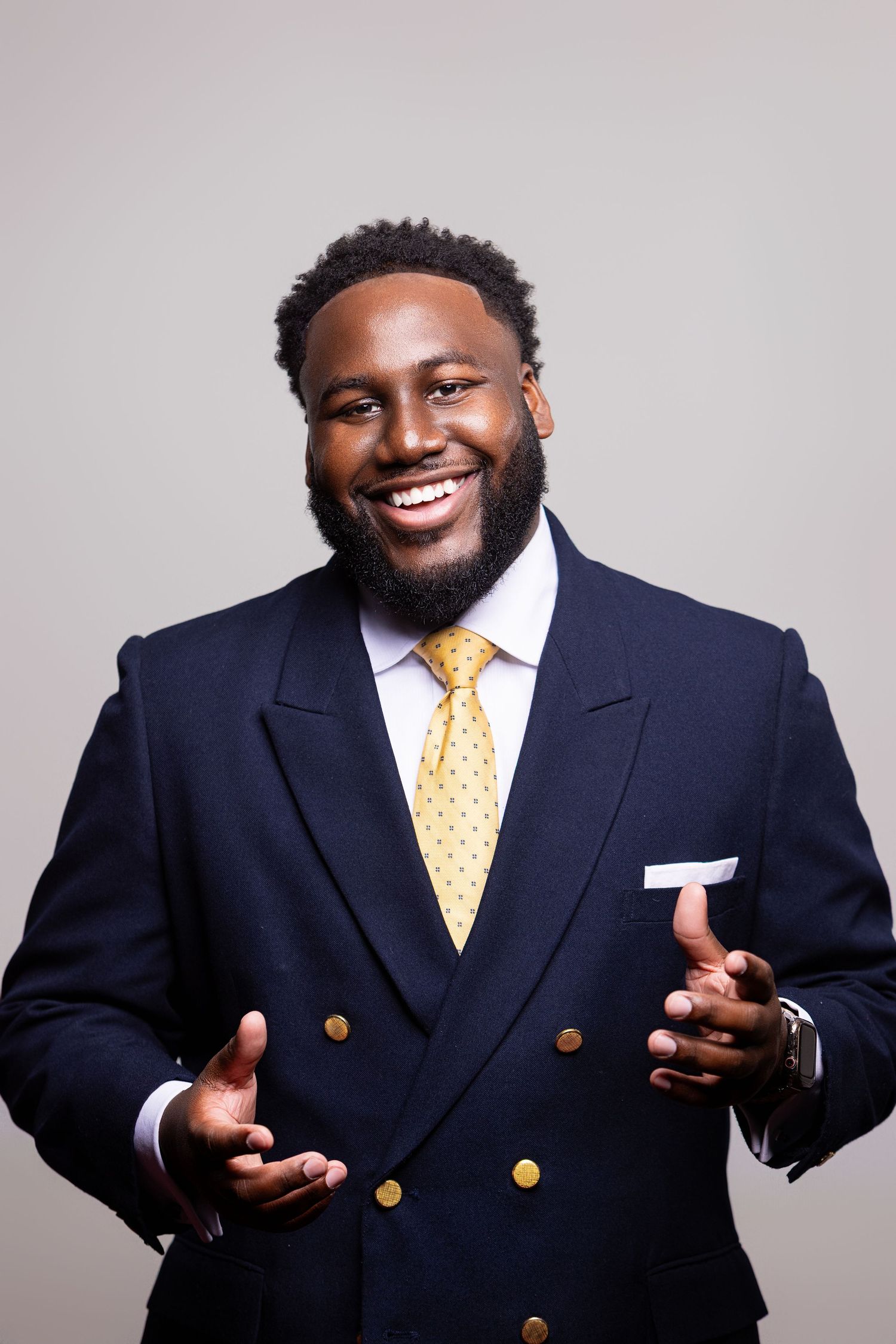 Professional portrait series showing a navy suit and yellow tie against a light gray studio background.