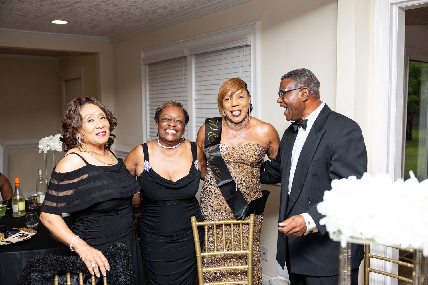 Four elegantly dressed guests socializing at a formal black-tie event in a decorated venue.