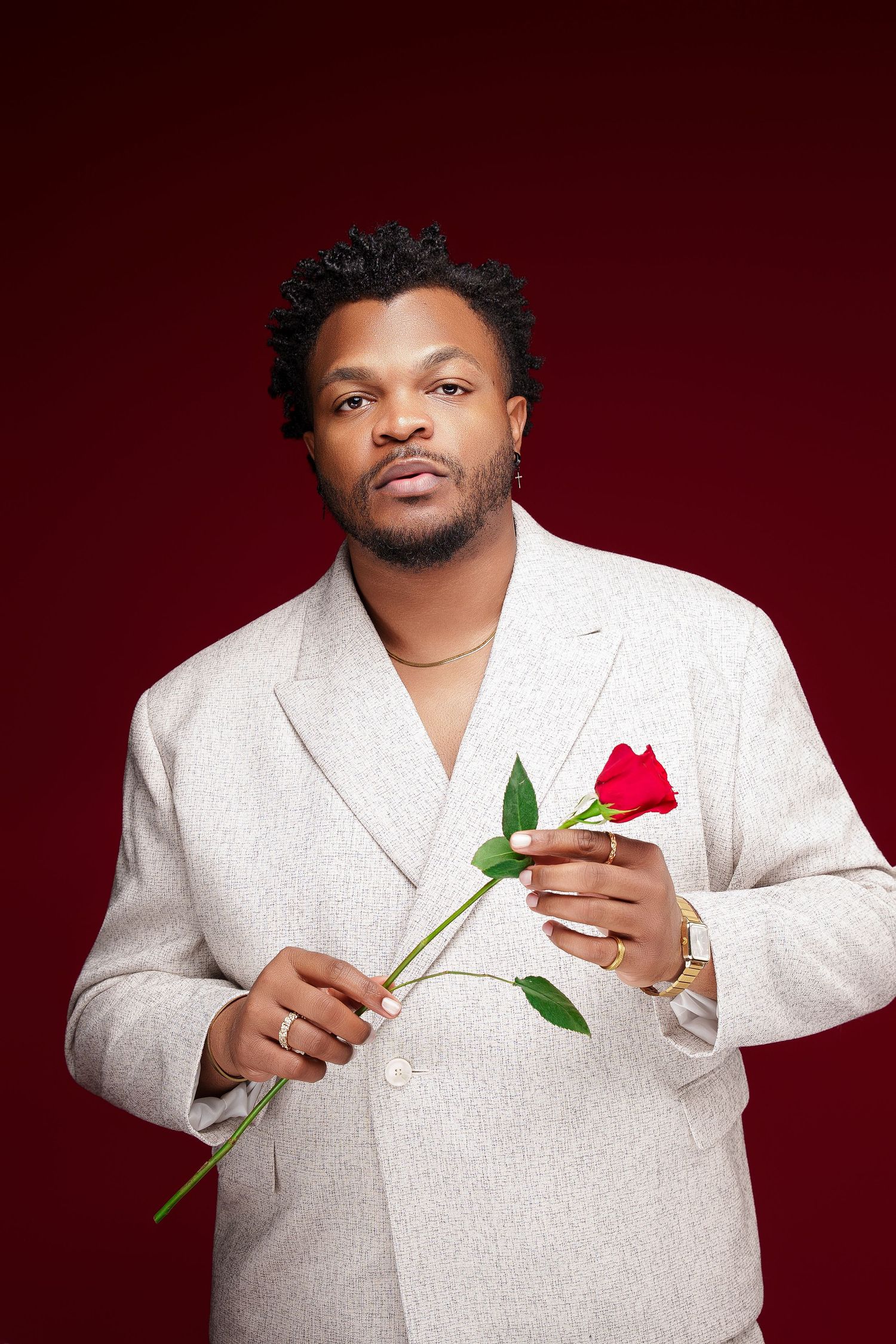 A person in a white suit jacket holds a red rose against a deep burgundy background in a romantic portrait series.