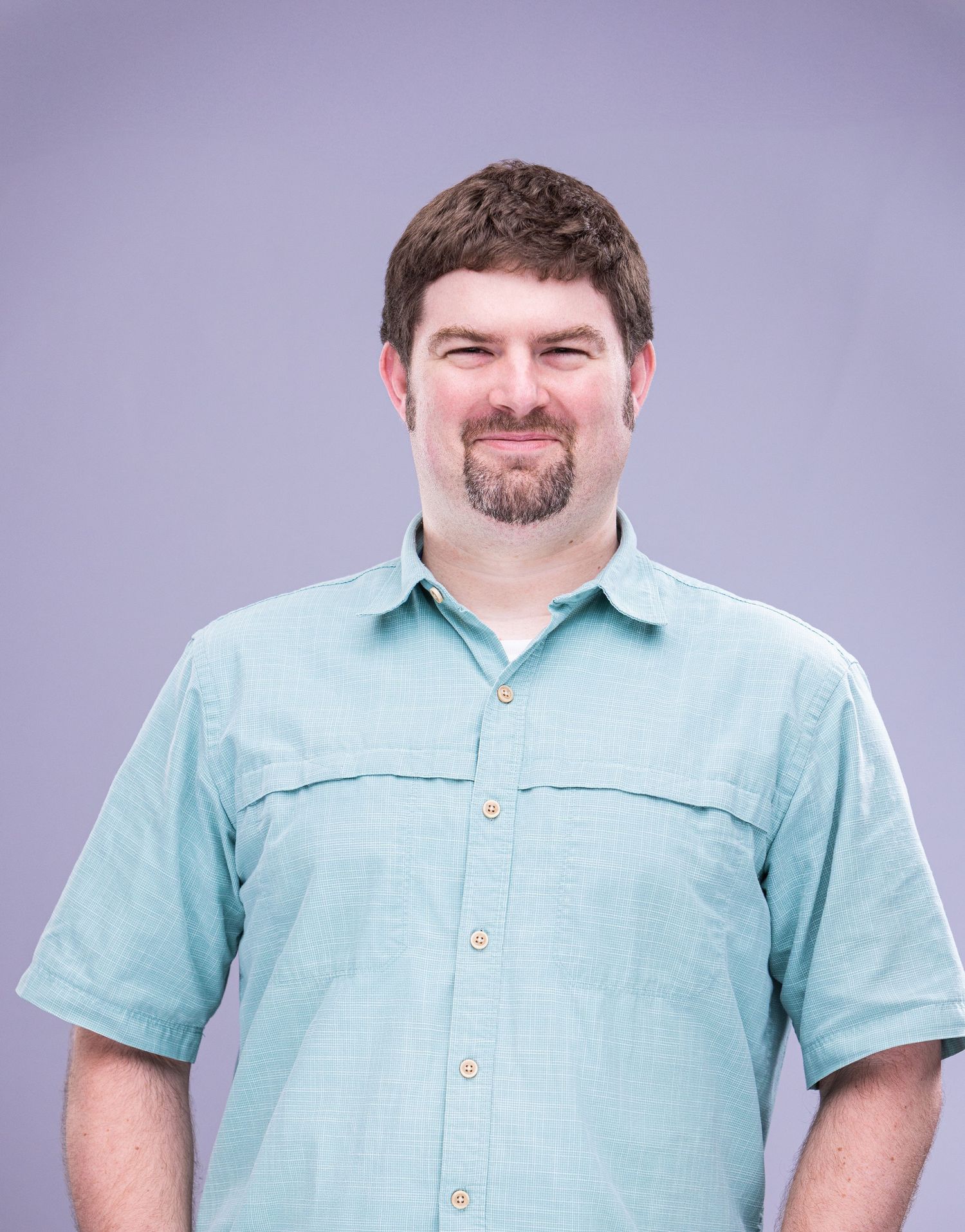 Professional portrait of person in light blue short-sleeve button-down shirt against purple background.
