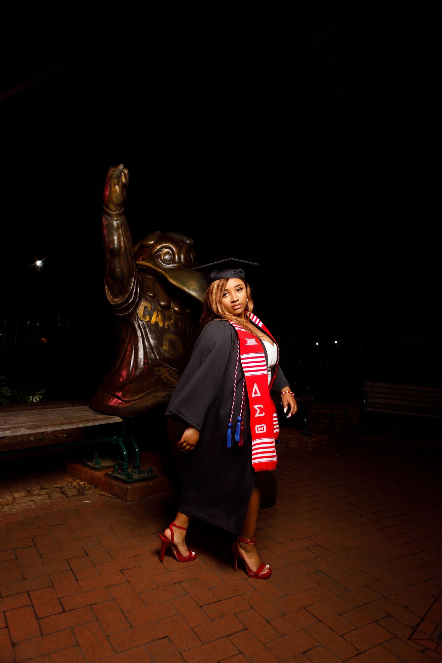 Dramatic nighttime graduation portraits featuring academic regalia and red scarf against dark background.