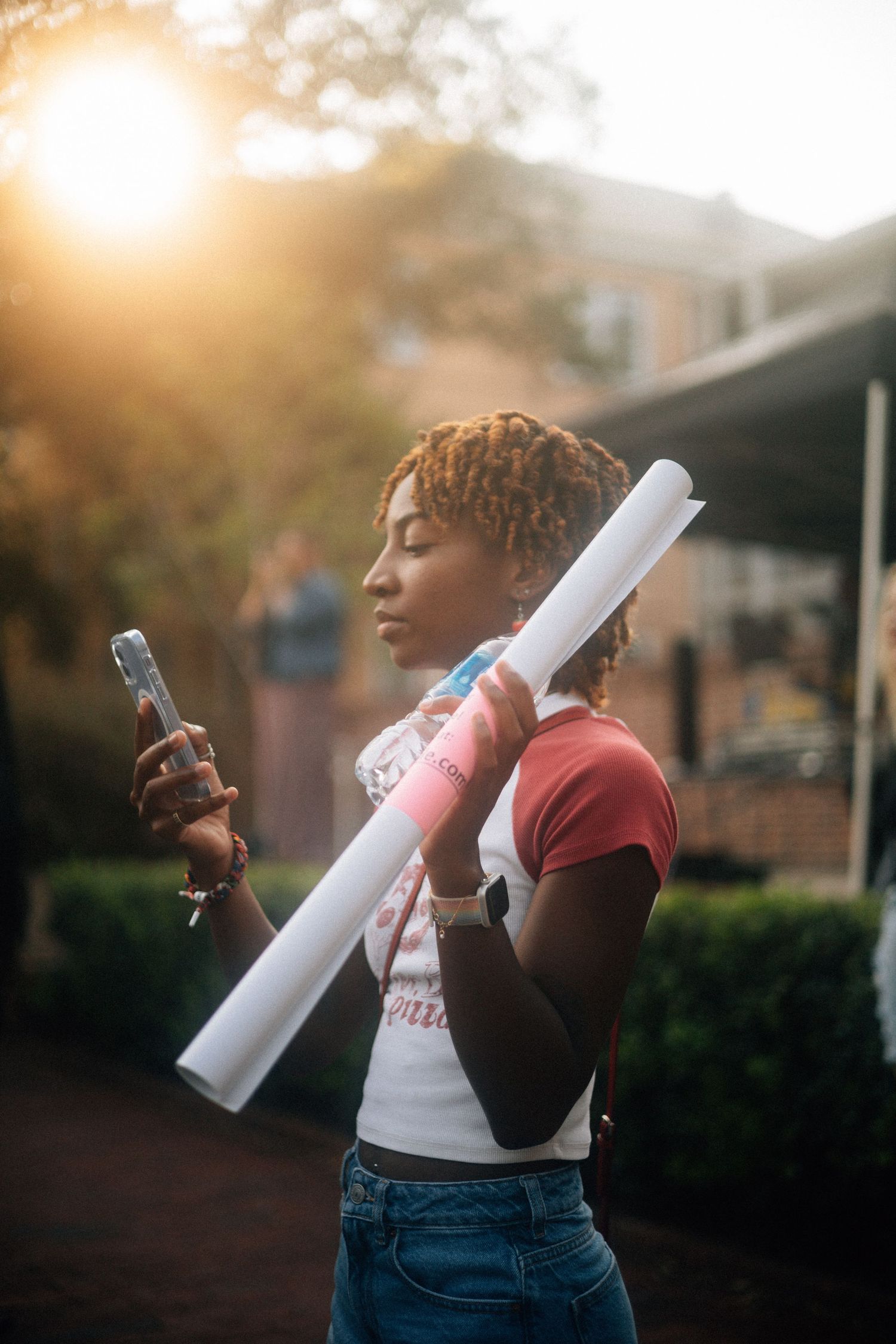 A recent graduate holding a diploma and phone stands in golden sunlight during a heartfelt outdoor photoshoot. USC Hip Hop Wednesday