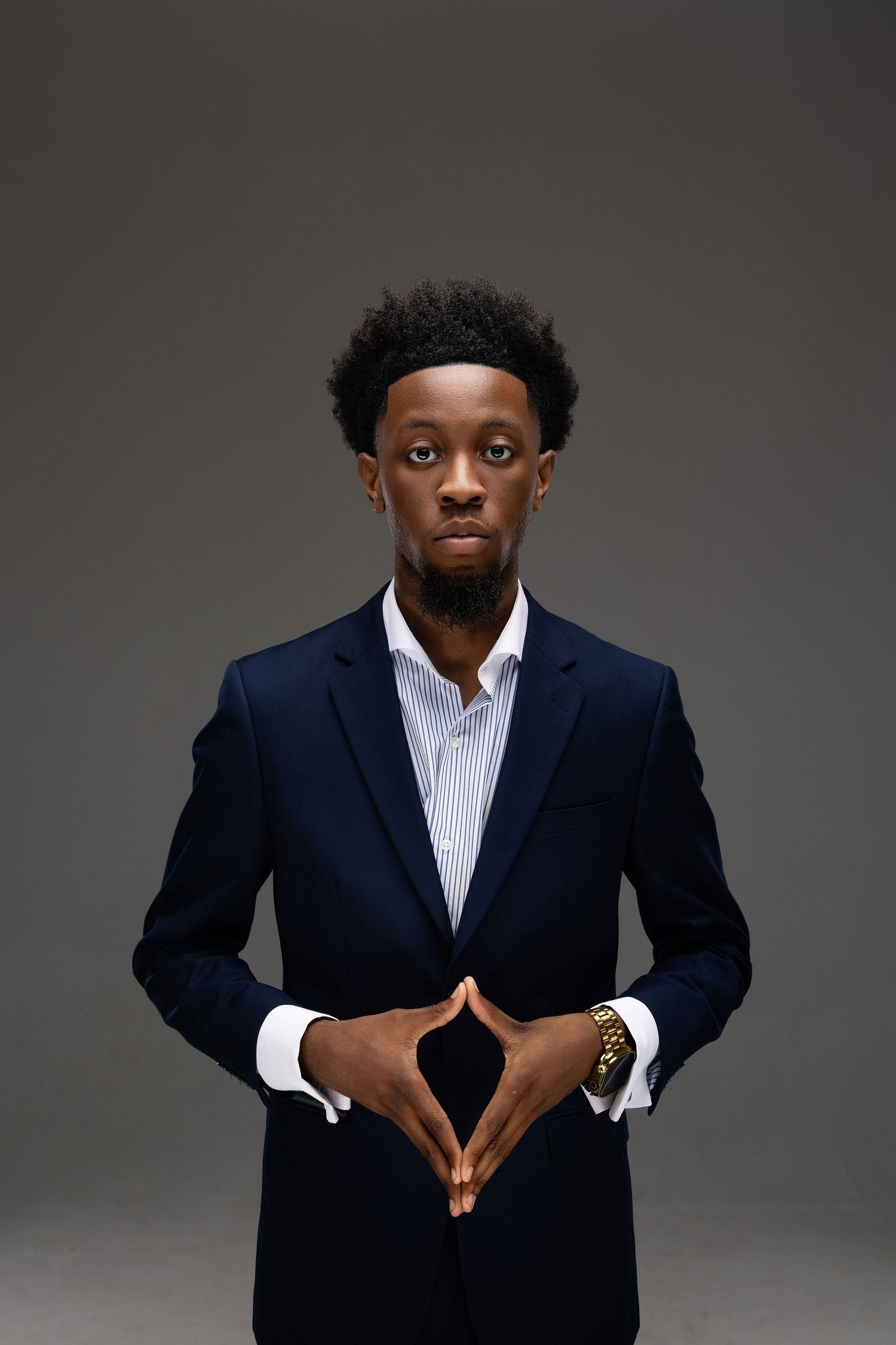 Professional studio portrait showing hands adjusting a navy suit jacket against a gray background.