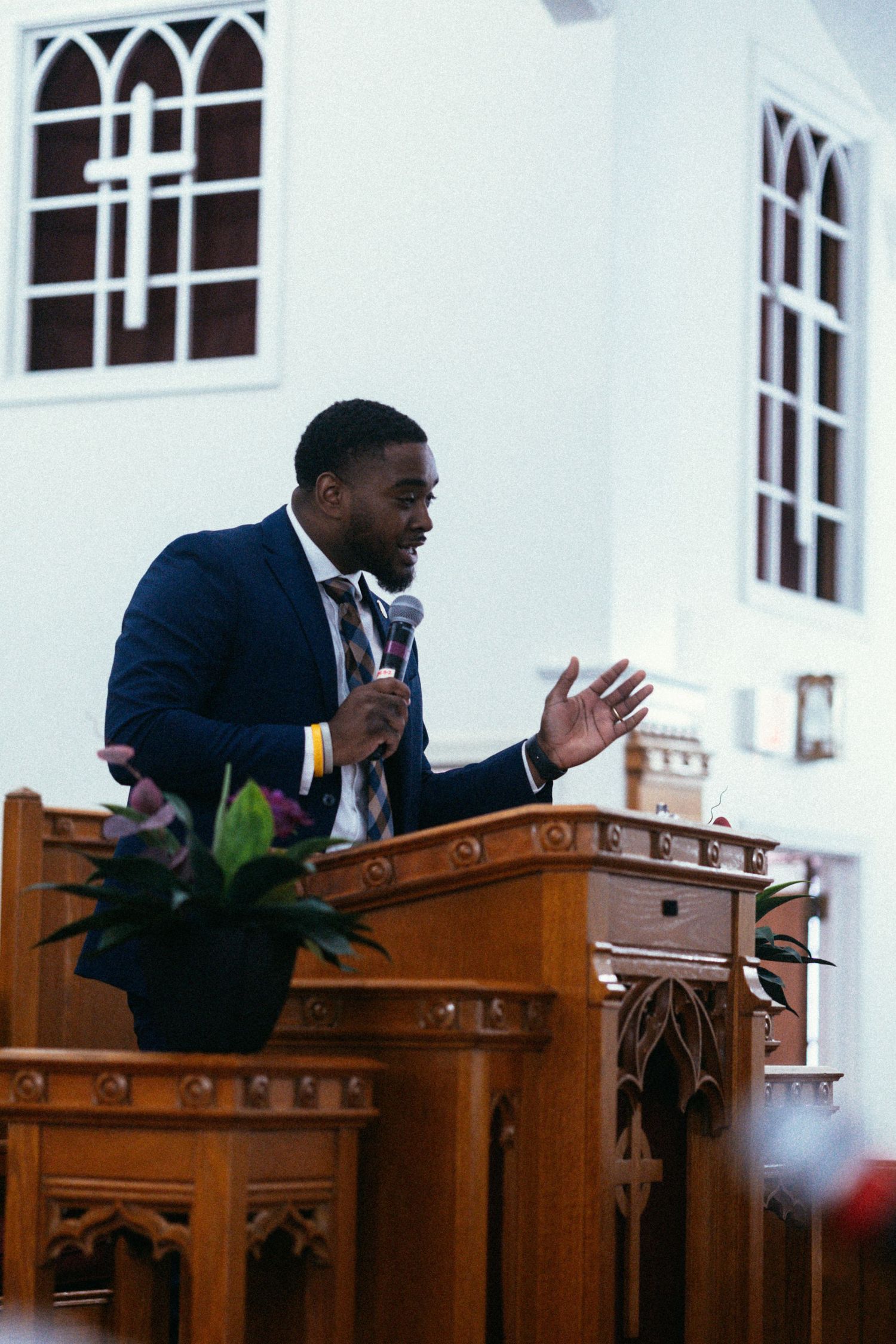 A speaker delivers a message from behind an ornate wooden church pulpit with decorative windows visible.