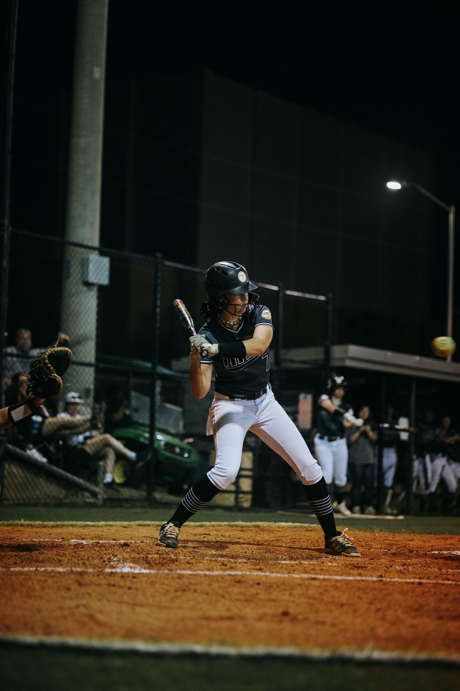 Baseball player in batting stance on dirt field under night game lights.