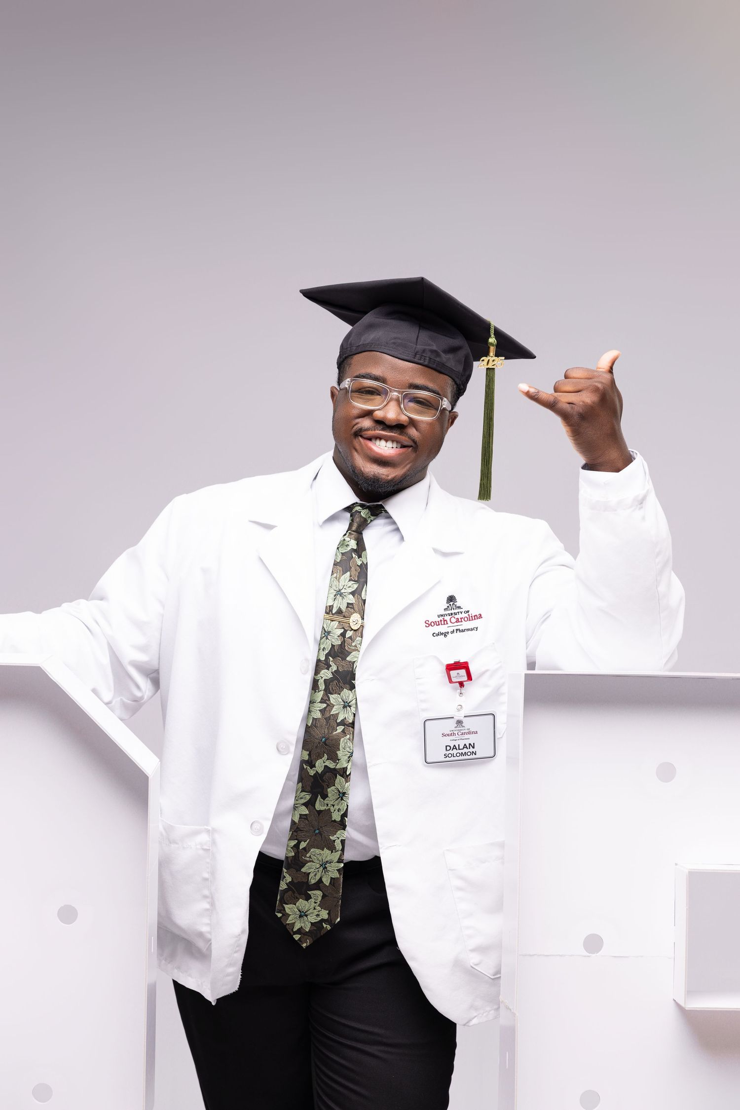 Graduate in white medical coat and graduation cap posing against light background.