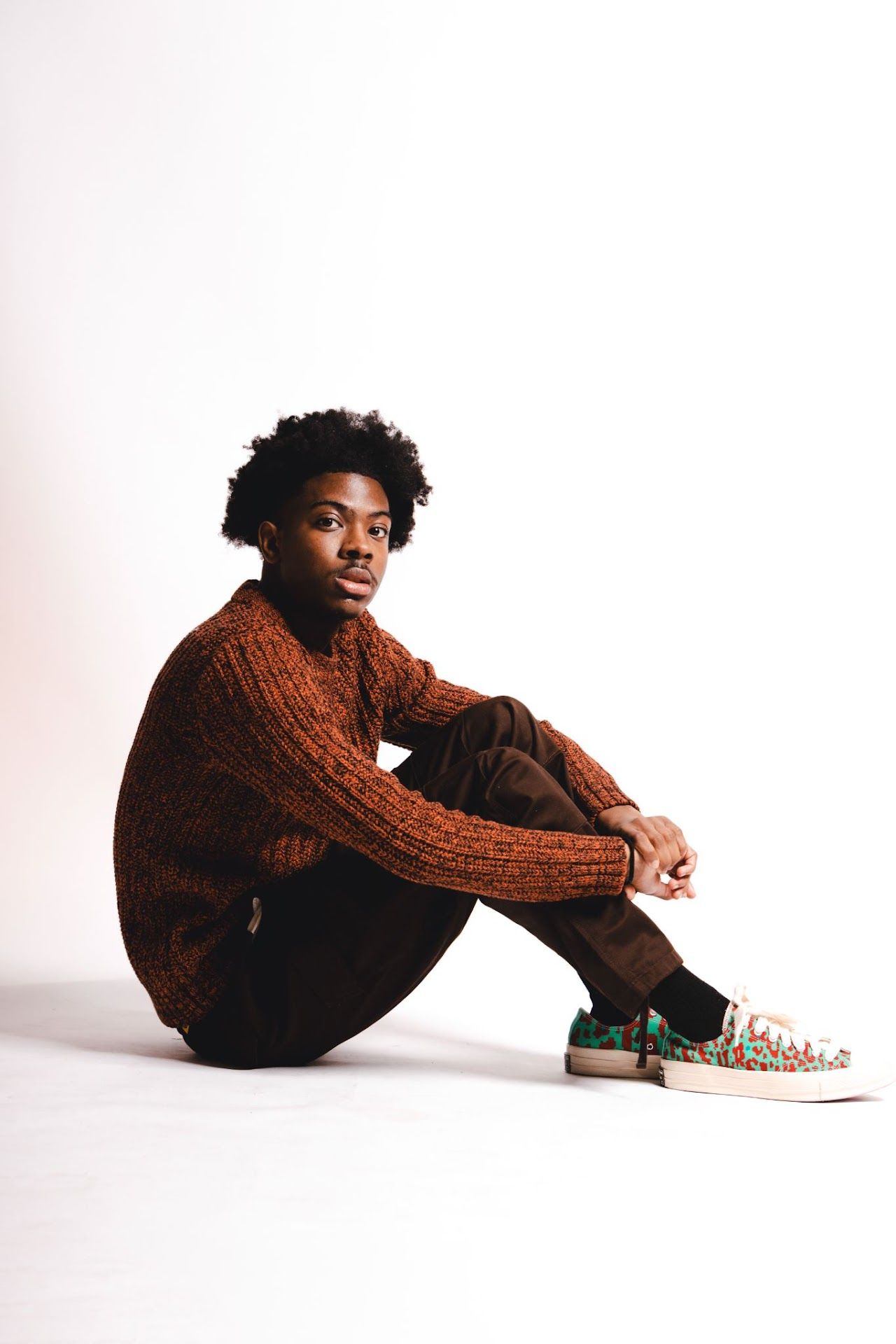 Artistic photo series showing a person in a brown sweater sitting in different poses against a white background.