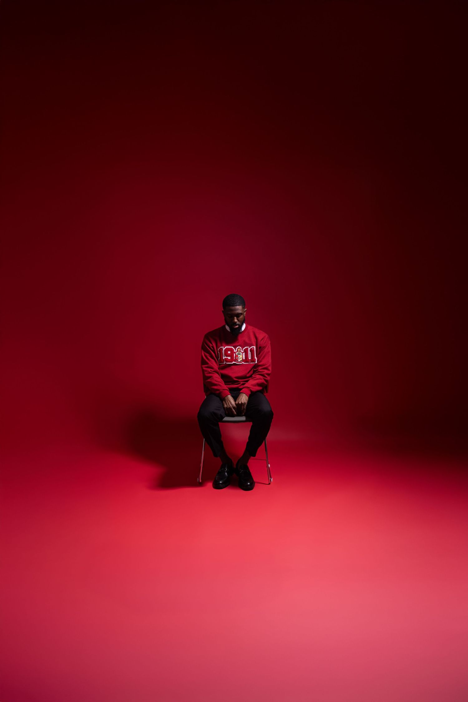 Person in red clothing sitting on chair against dramatic red backdrop in studio setting.