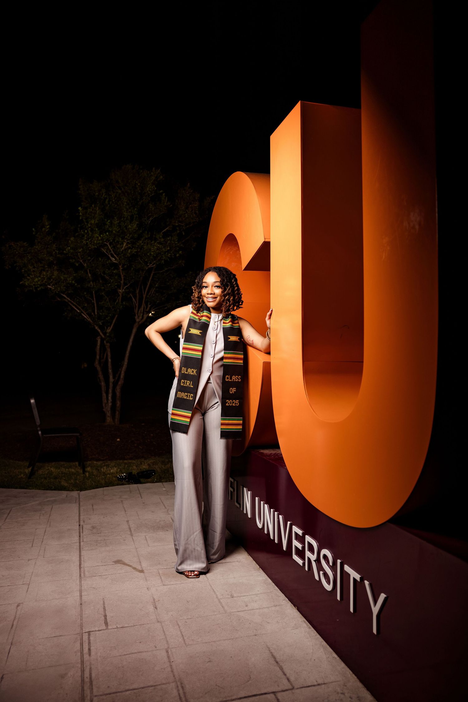 Stylish figure poses against illuminated orange university signage at night.