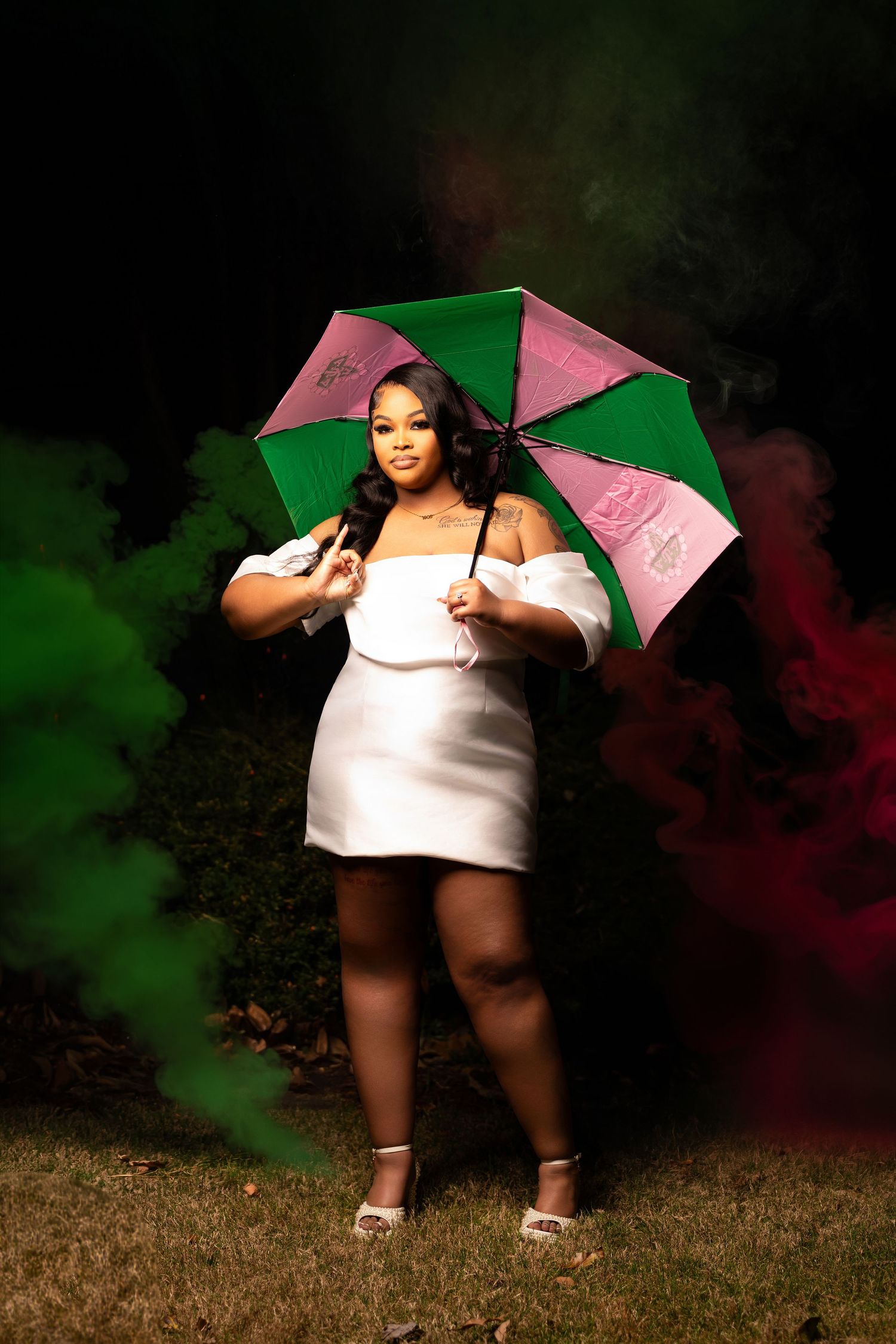 A person in a white dress poses with a pink and green umbrella in an artistic outdoor AKA photoshoot series.