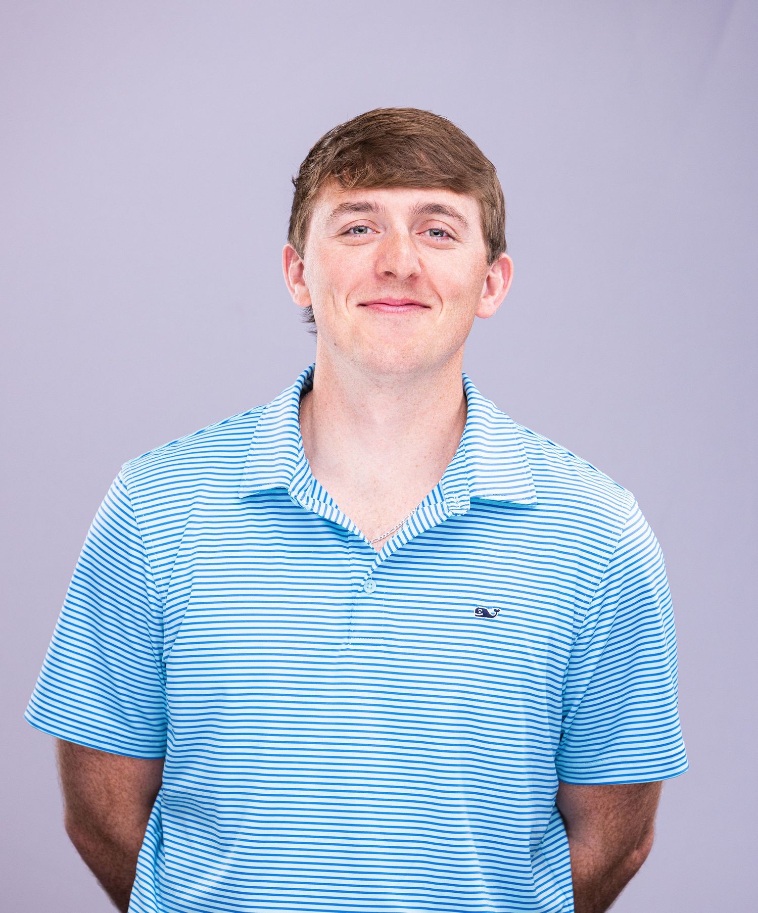 Professional headshot of person in blue and white striped polo shirt against purple background.