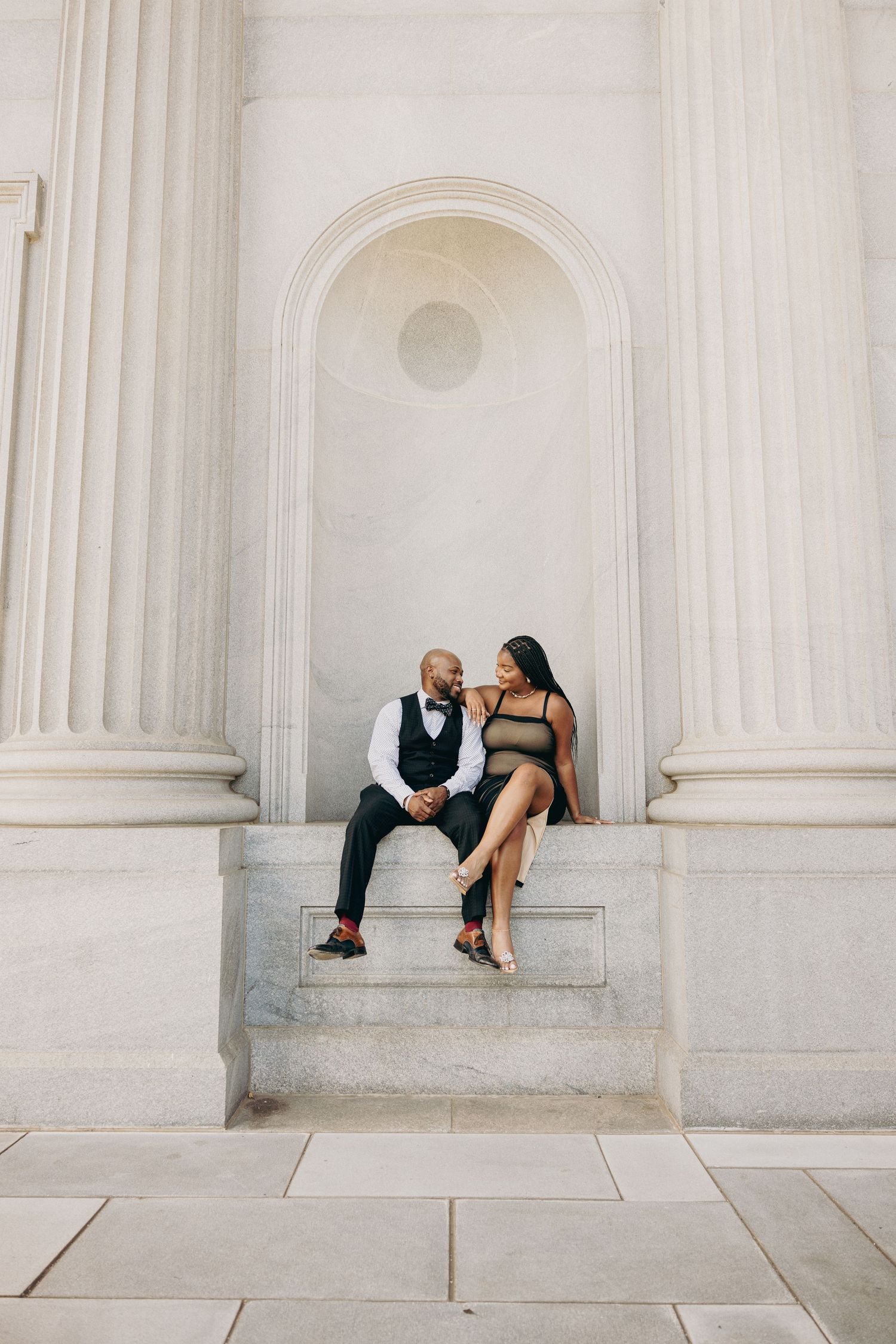 Romantic couple poses intimately against white classical architecture columns.