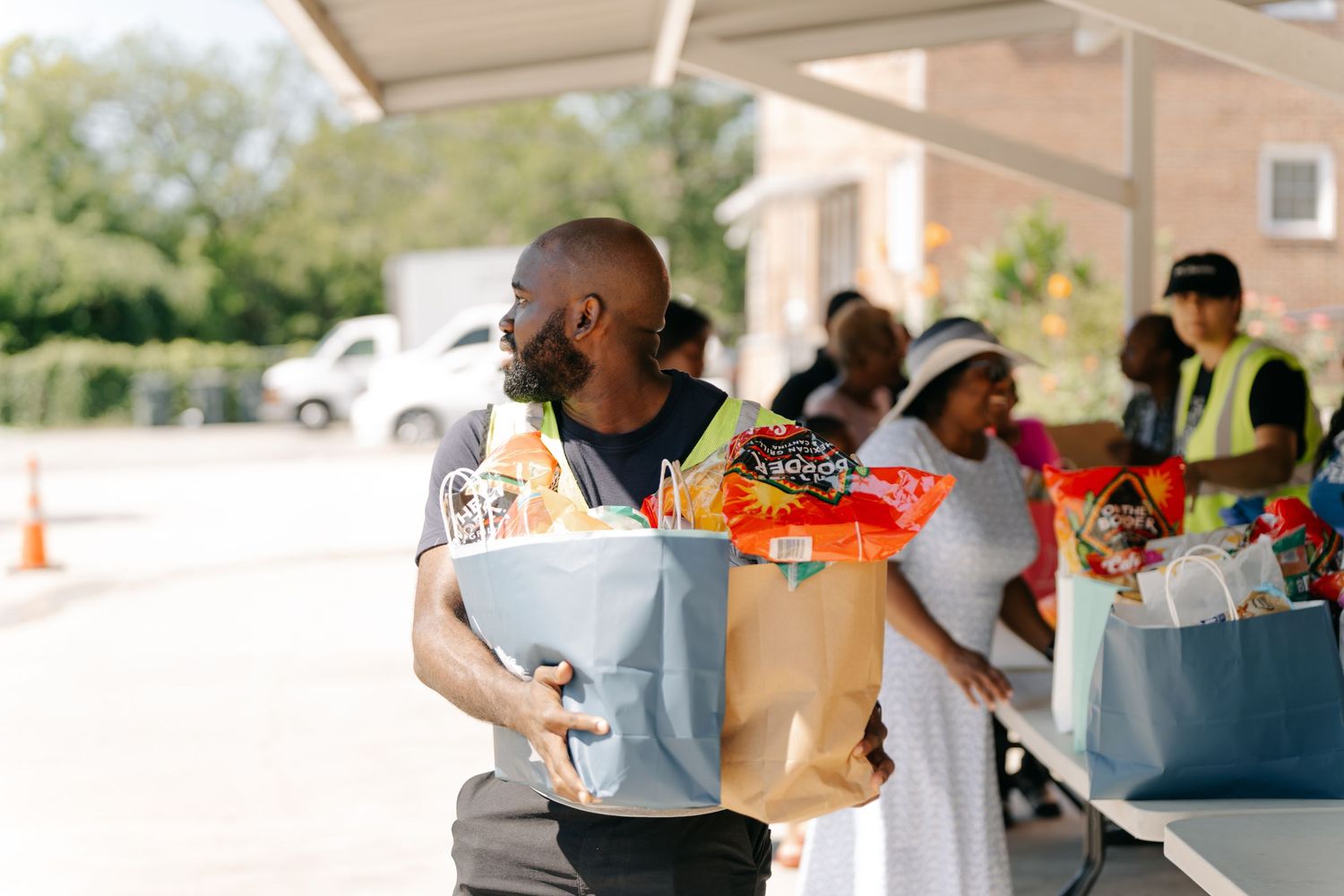 Man carrying grocery bags filled with food donations at an outdoor community food distribution event.