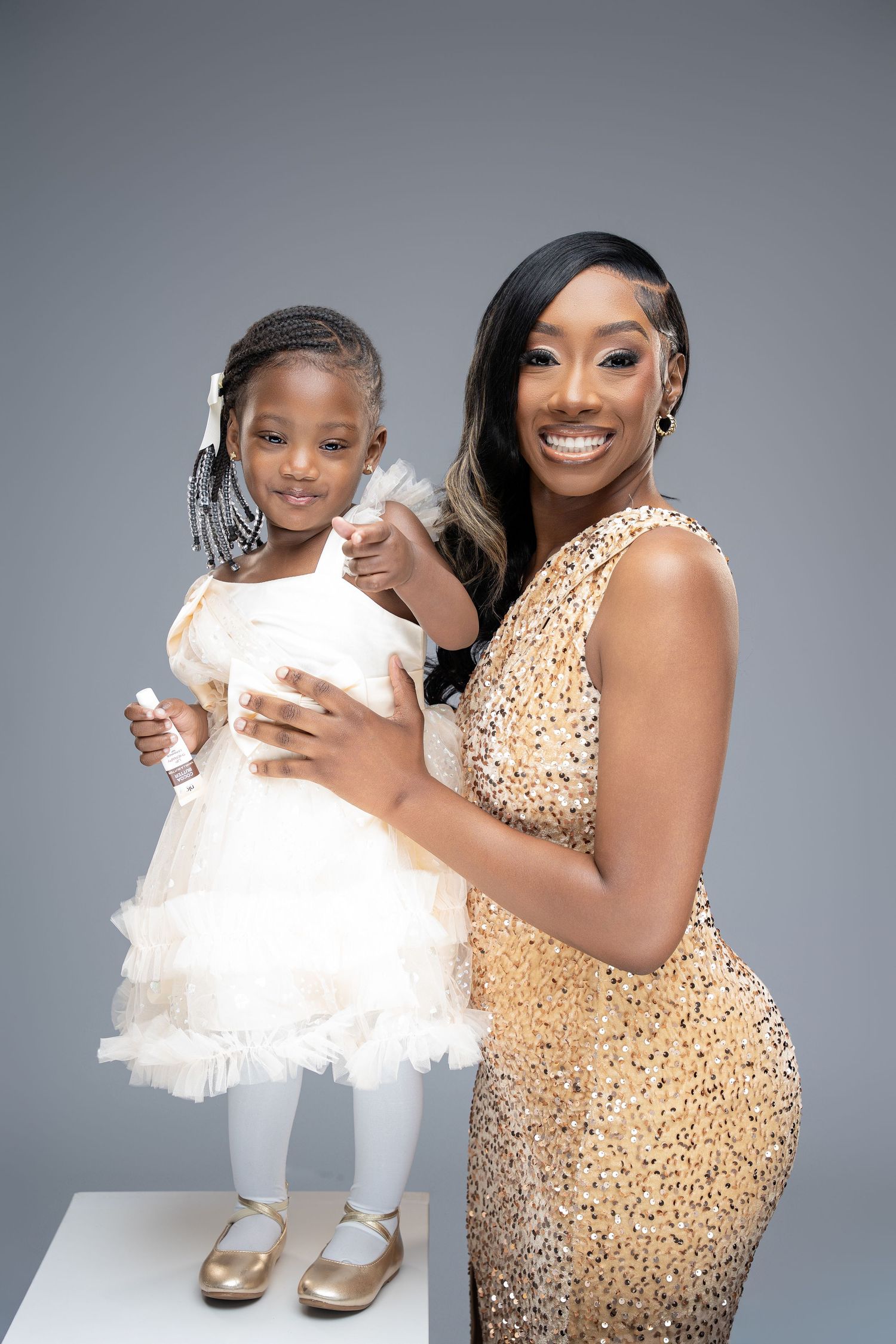 A mother and daughter share a joyful moment in matching gold and white formal attire during a studio photoshoot.