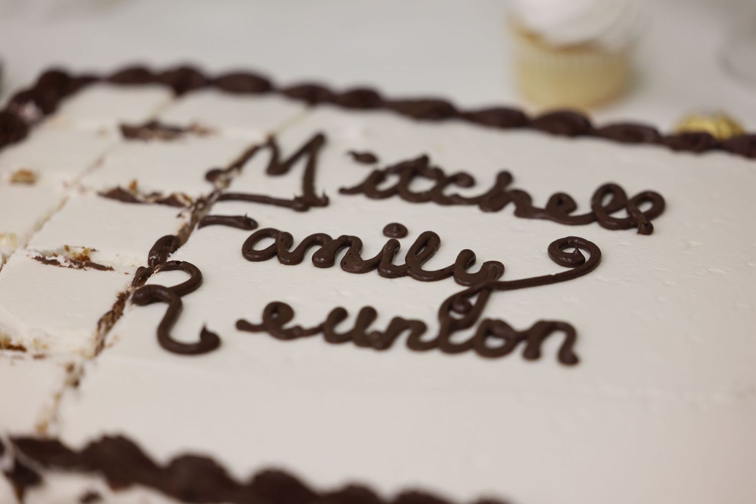 White sheet cake decorated with chocolate script reading Mitchell Family Reunion for a celebratory gathering.