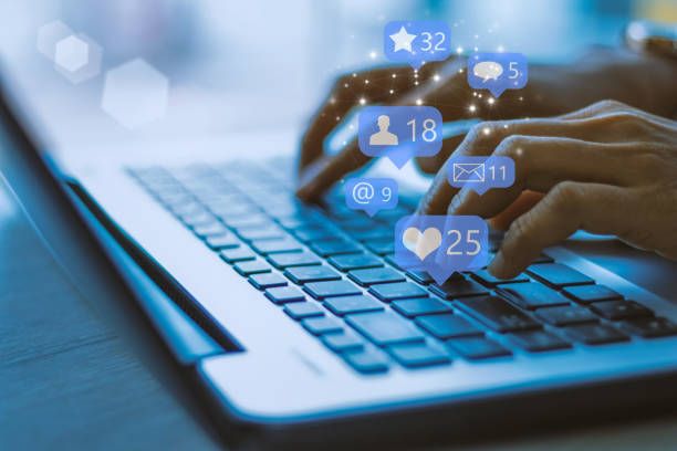 Hands typing on laptop keyboard with floating social media engagement icons showing likes, comments and shares.