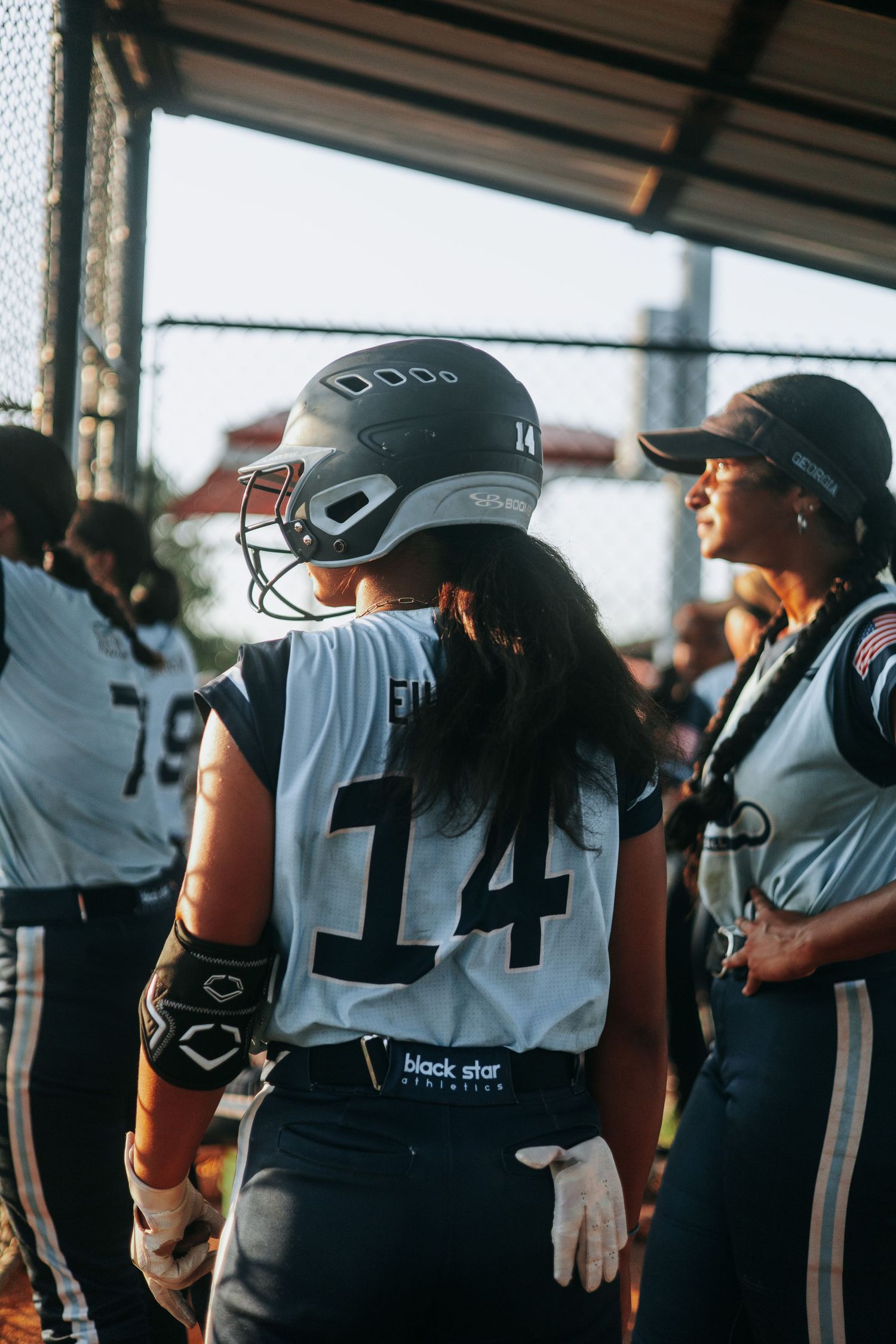 Softball players in uniforms line up in the dugout during a game.