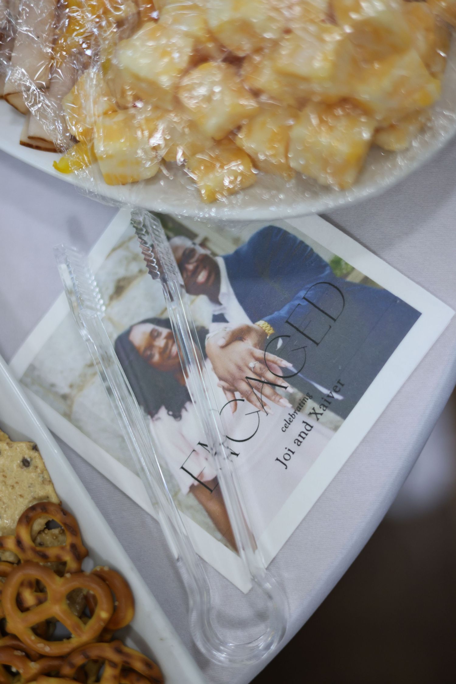 Wedding reception table with pretzels, desserts, tongs, and a program booklet celebrating Joi and Xavier's engagement.