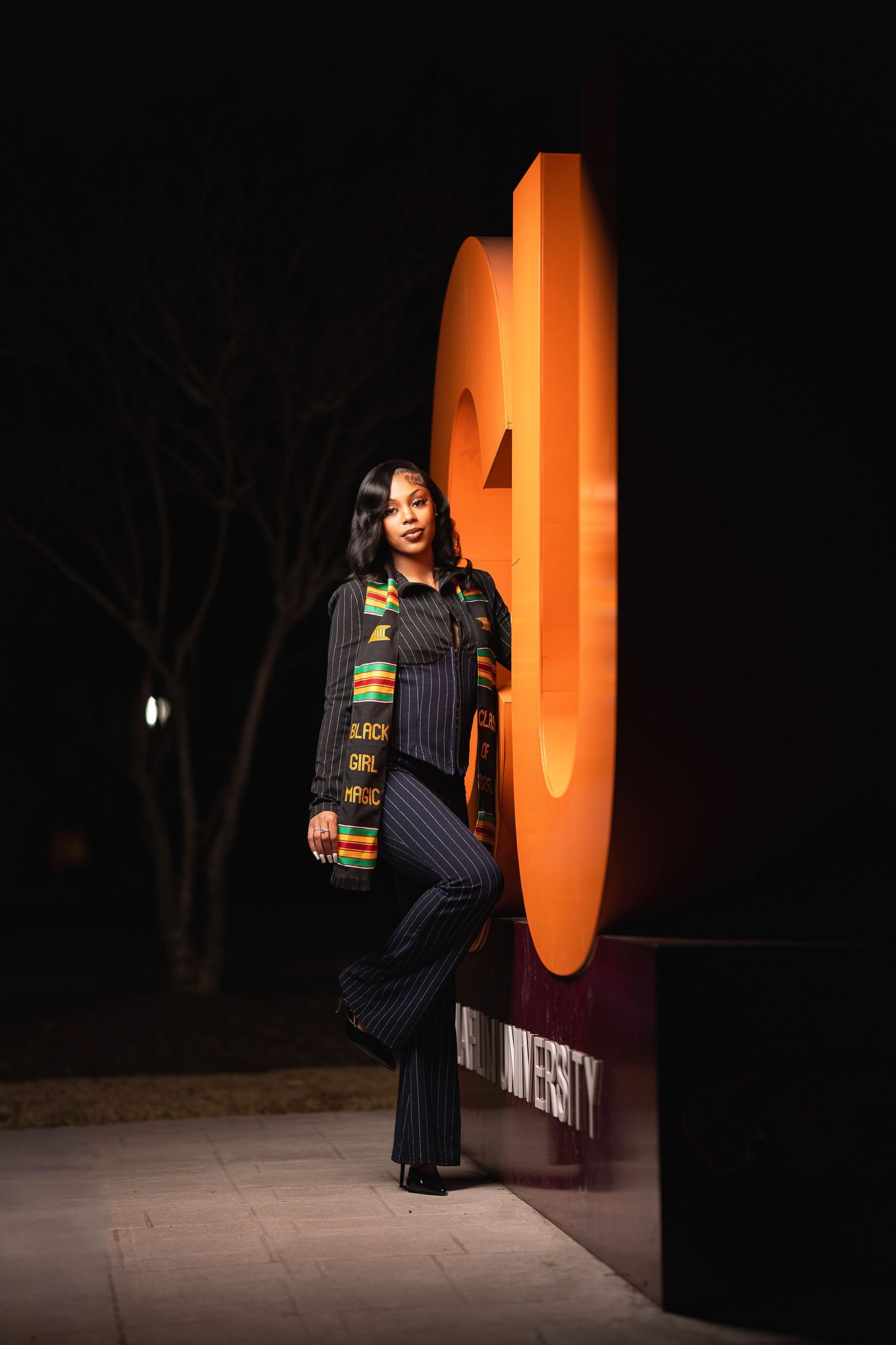 A fashion model poses in a pinstriped suit with African print details against an orange and black architectural backdrop.