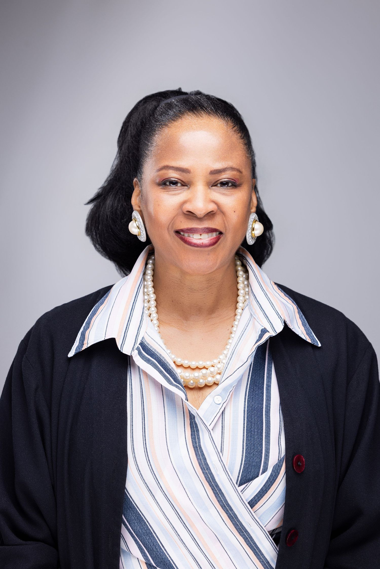 Professional headshot series showing a person in a black blazer and striped collared shirt with pearl necklace and earrings.