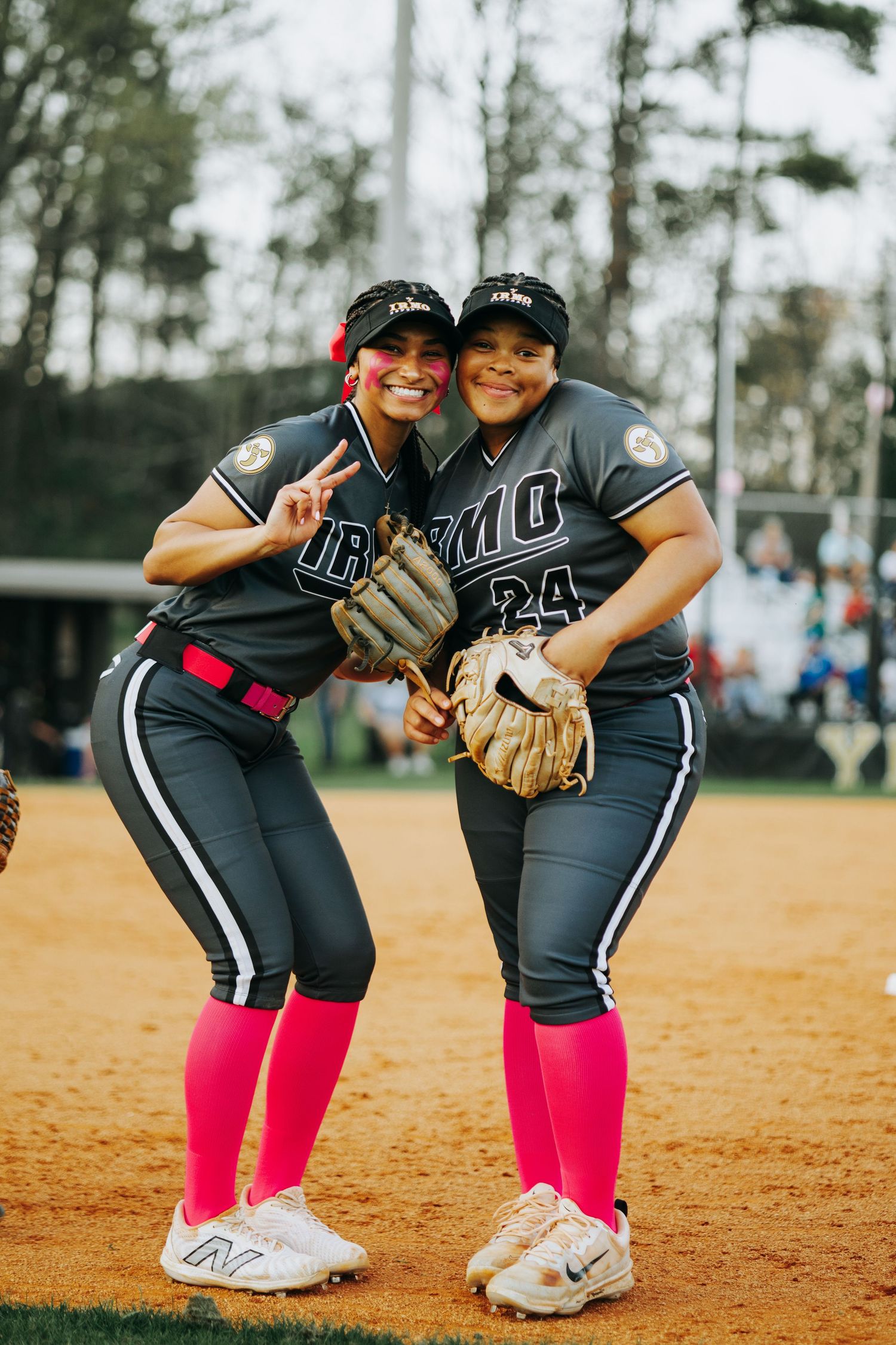 Two Irmo HS softball players in matching uniforms with pink socks pose playfully on the field.